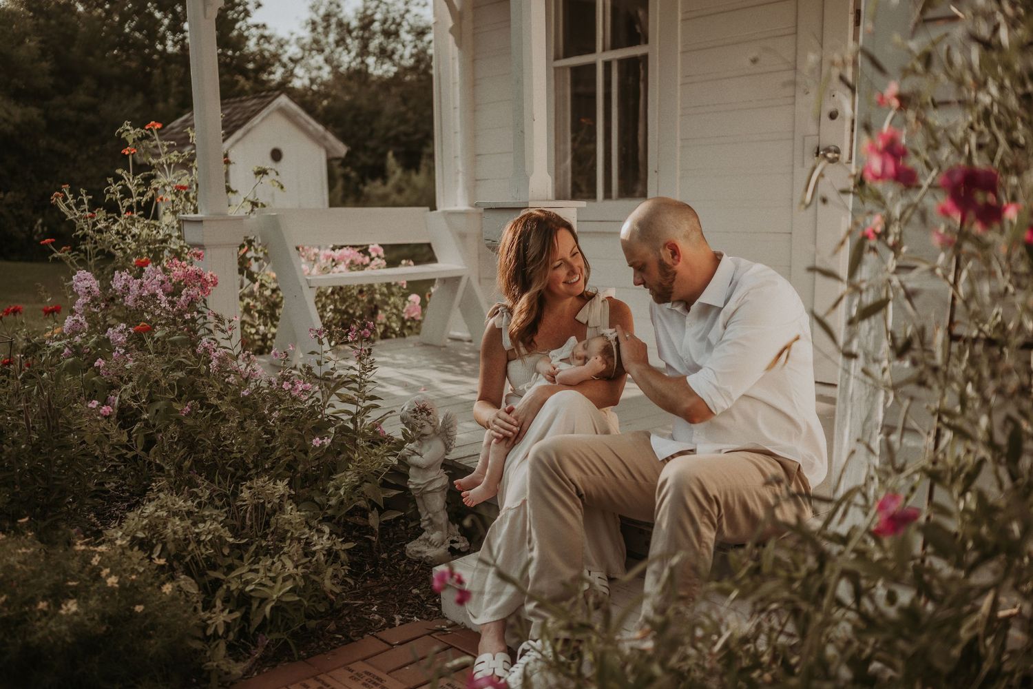 Golden hour portrait session on a charming farmhouse porch surrounded by blooming flowers.