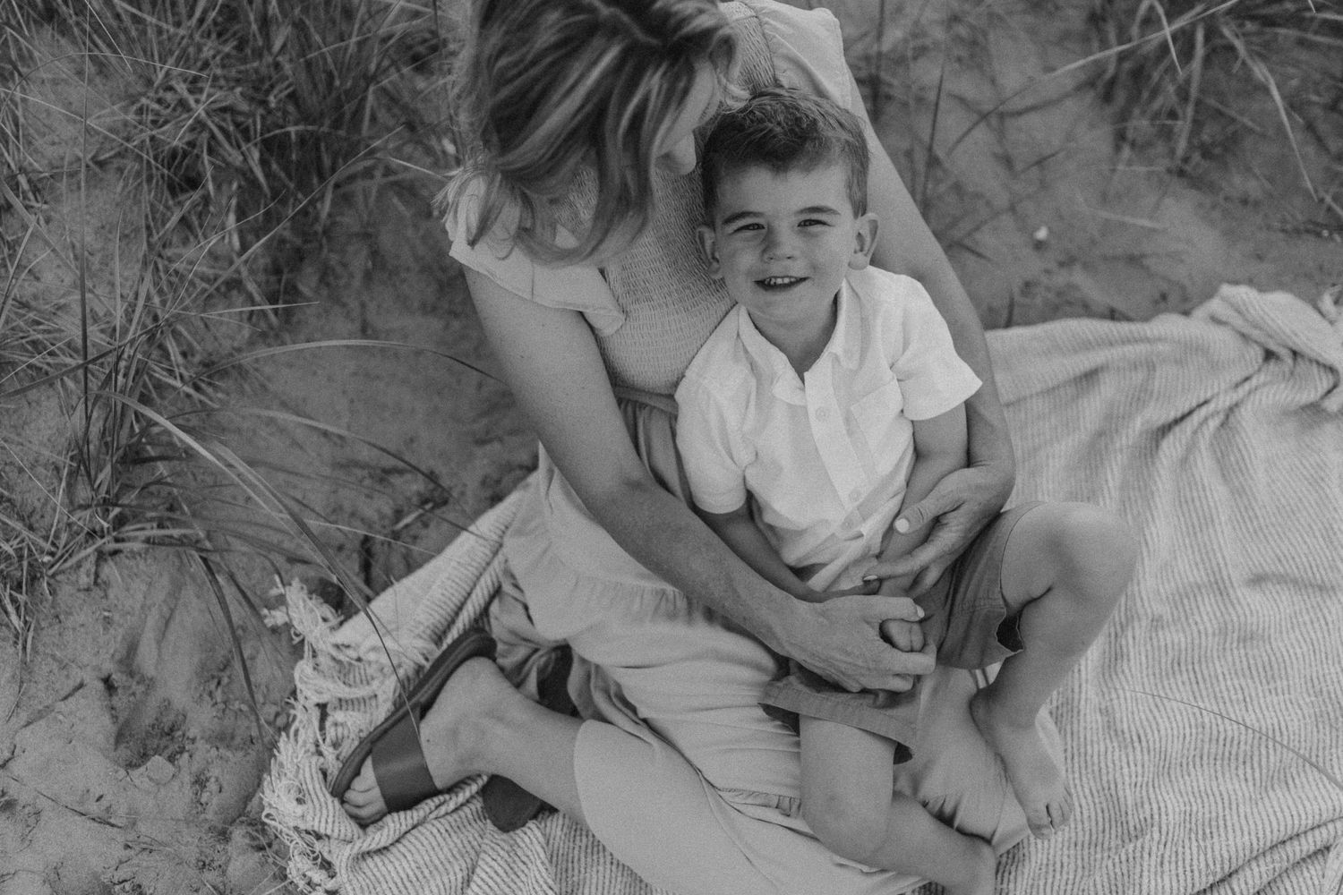 A black and white portrait of two people sharing a tender moment on a beach blanket.