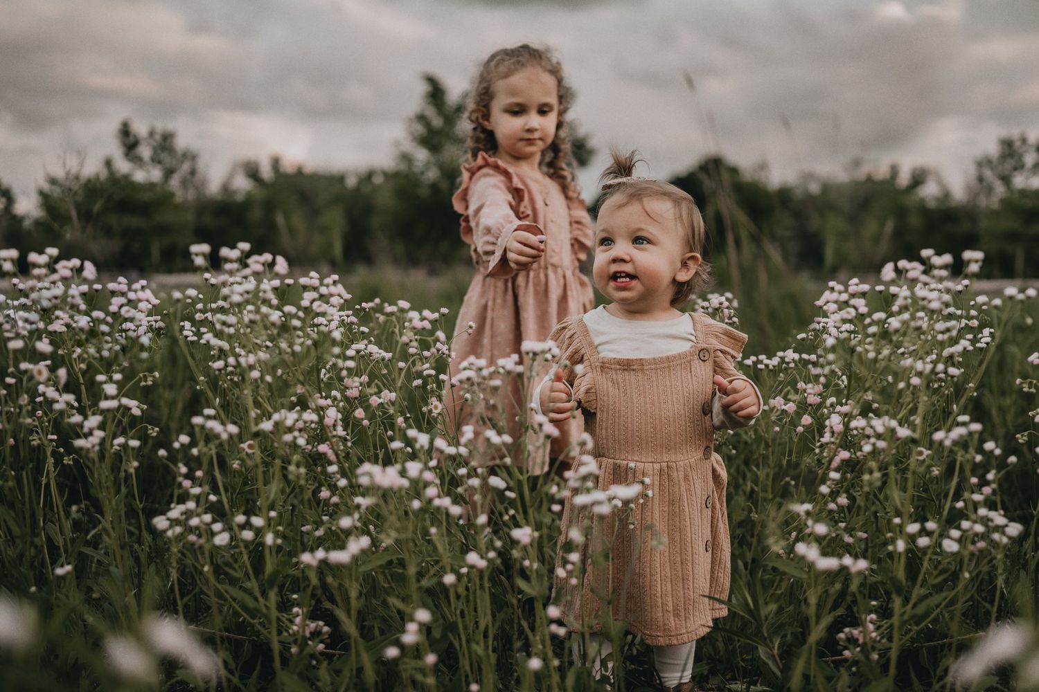 Two children in matching outfits stand together in a blooming daisy field at dusk.
