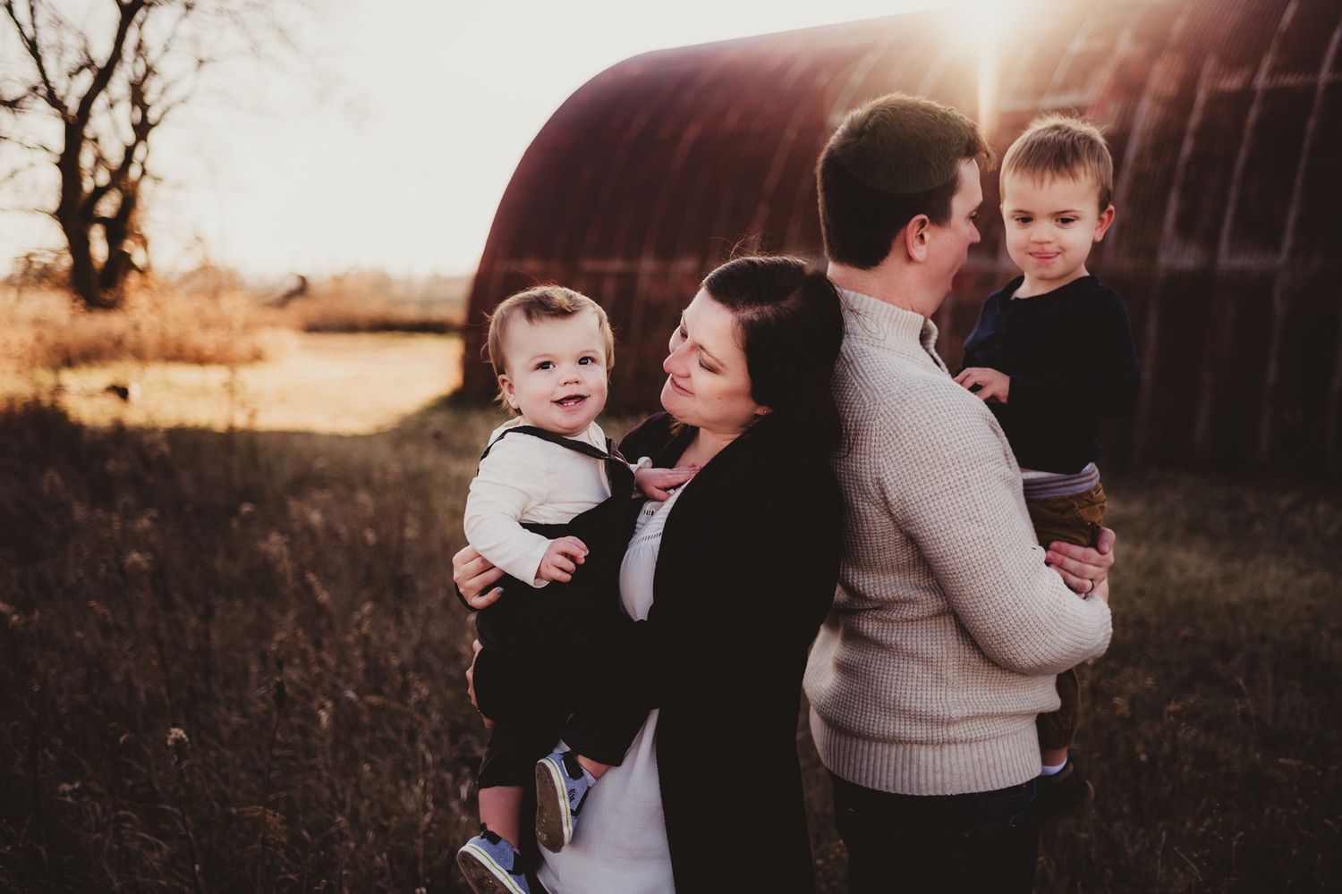 Candid family photo at sunset with rustic barn background.