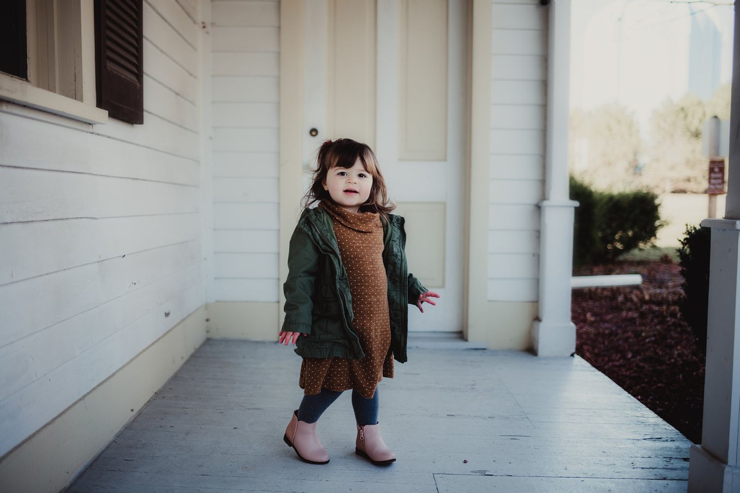 A child in autumn attire explores a white-columned porch with playful energy.