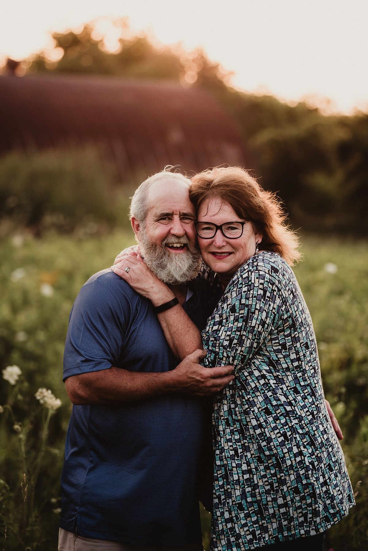 A mature couple embraces joyfully in a wildflower field during golden hour.