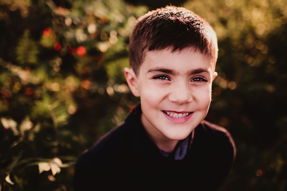 Portrait of young person in black shirt smiling against blurred nature background.