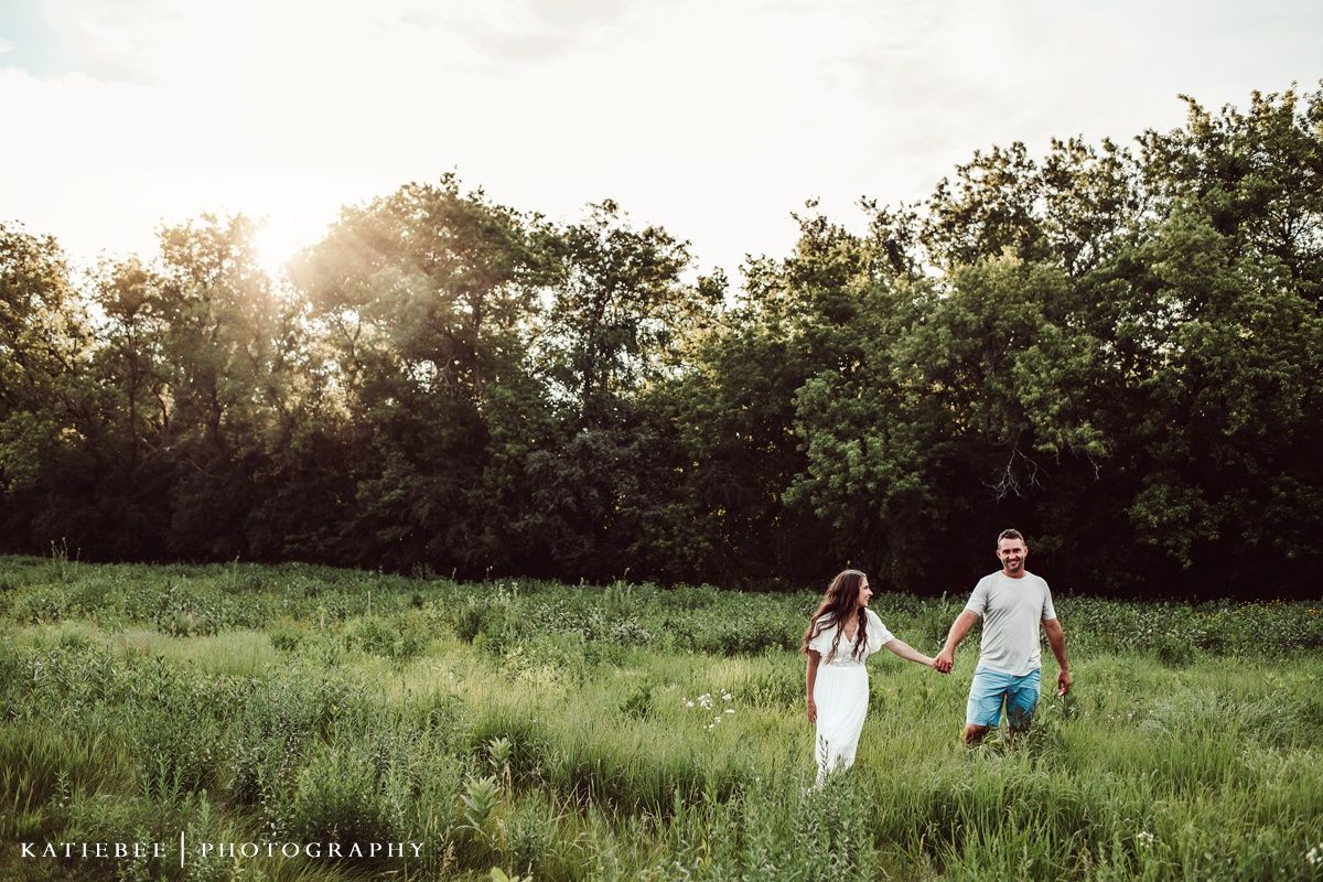 Couple walking hand in hand through sunlit meadow at golden hour.
