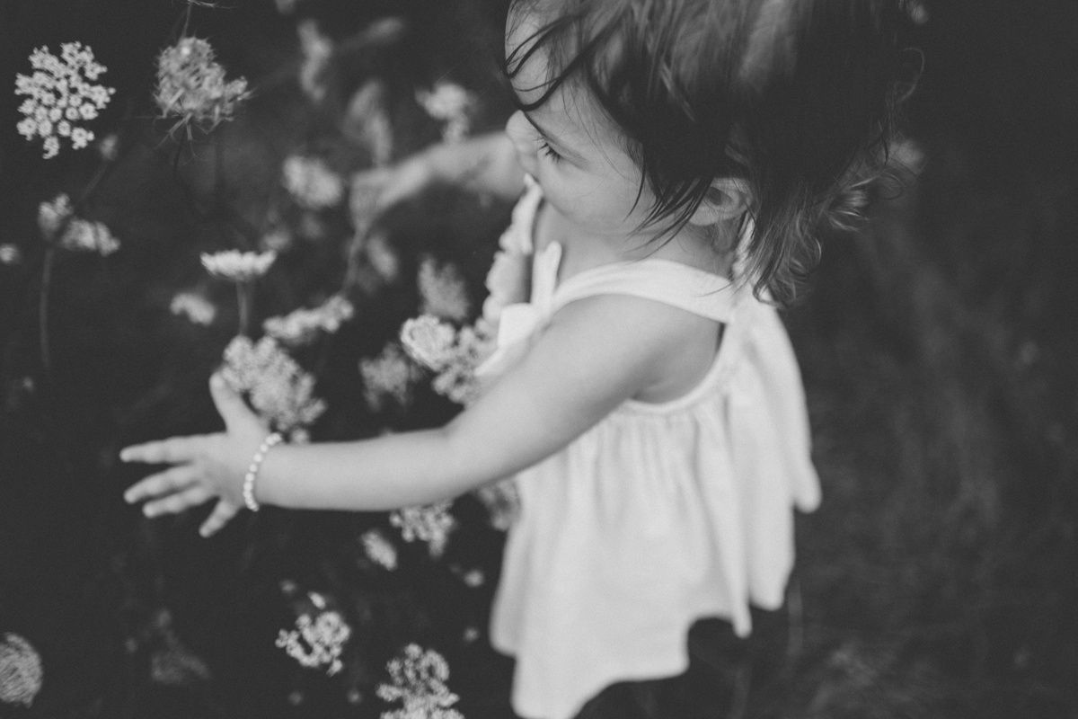 Black and white photo of small child reaching for flowers in garden.
