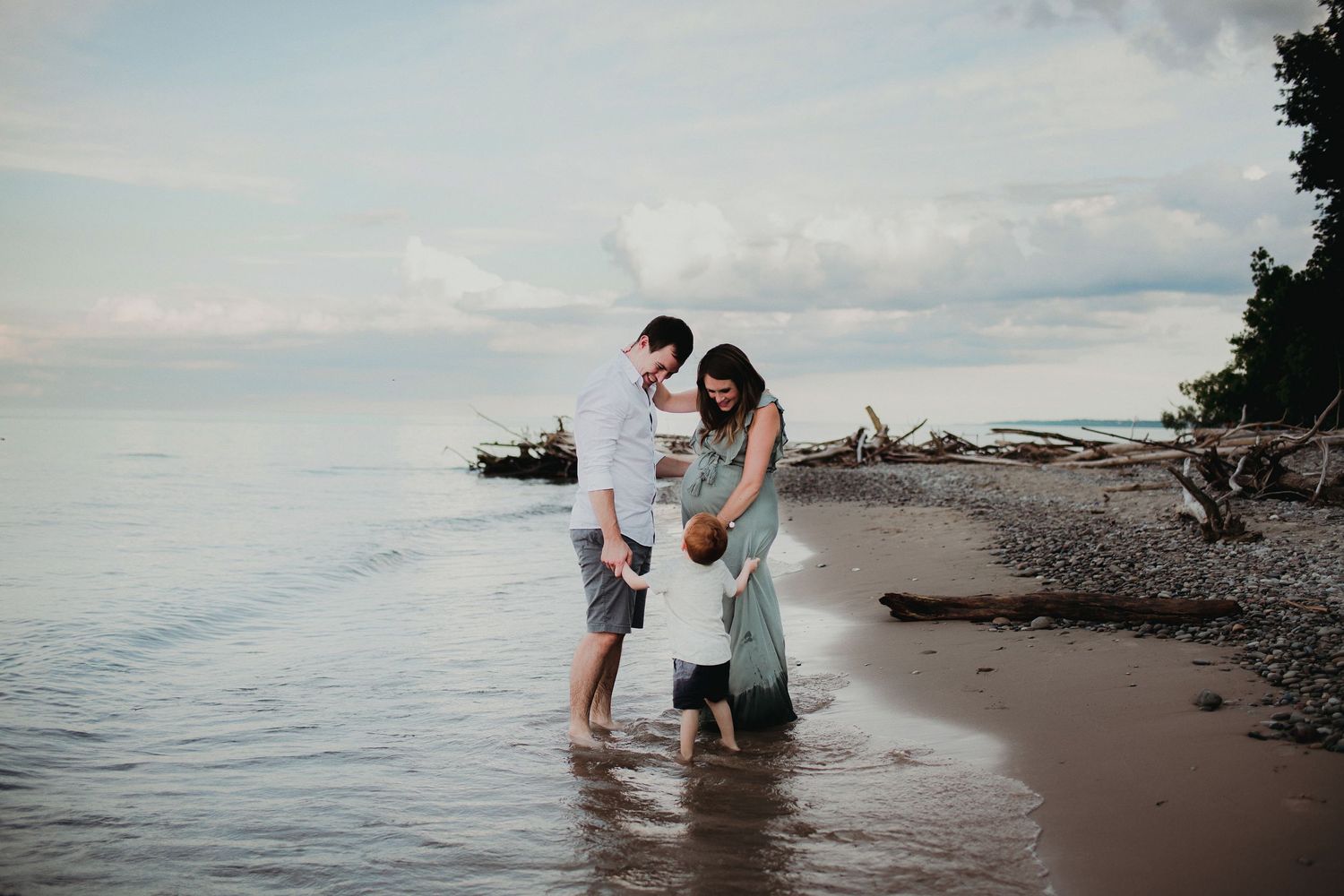 A family shares a tender moment together at the water's edge on a cloudy beach day.