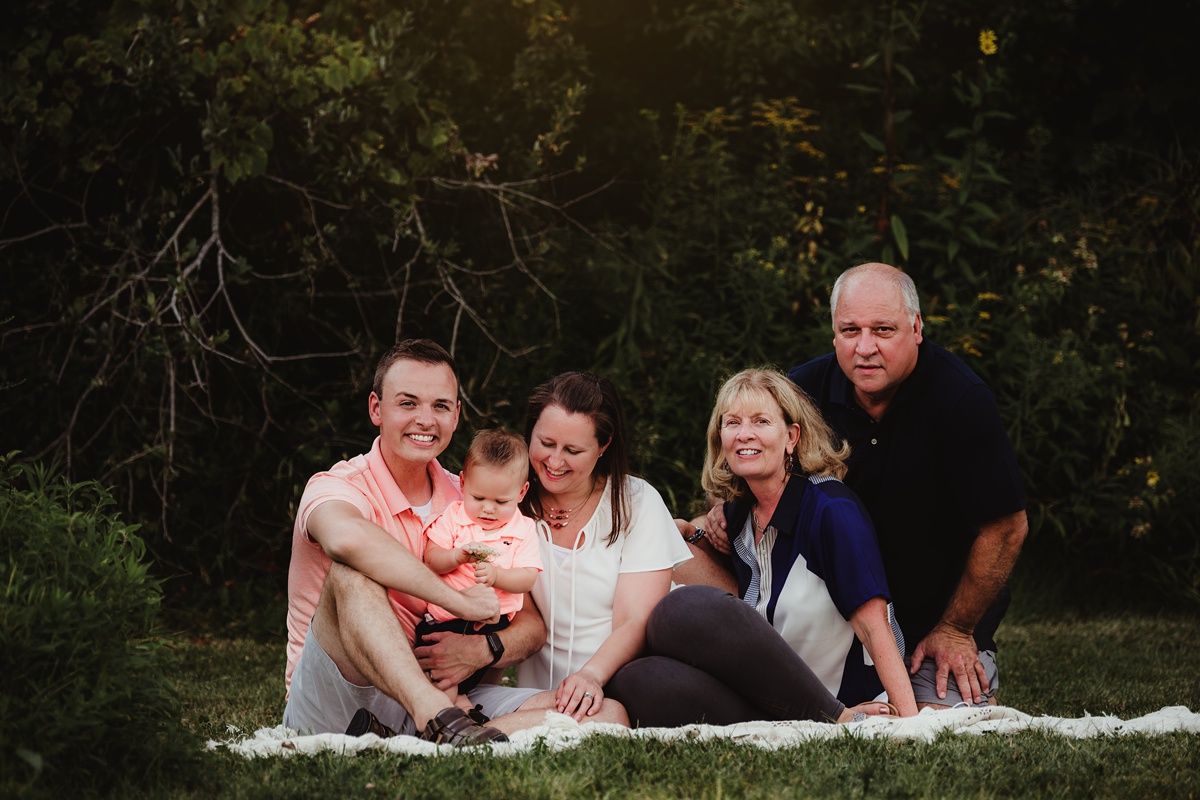 Extended family relaxing together on white blanket during outdoor photo shoot.