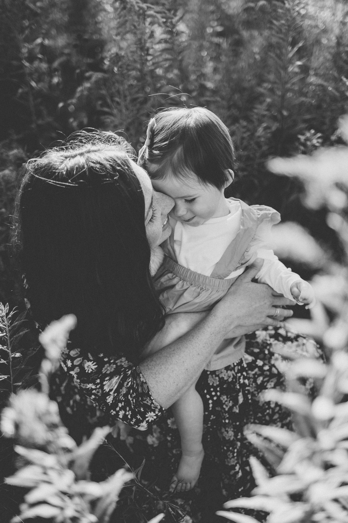 A tender black and white portrait of a parent holding a child in a garden setting.