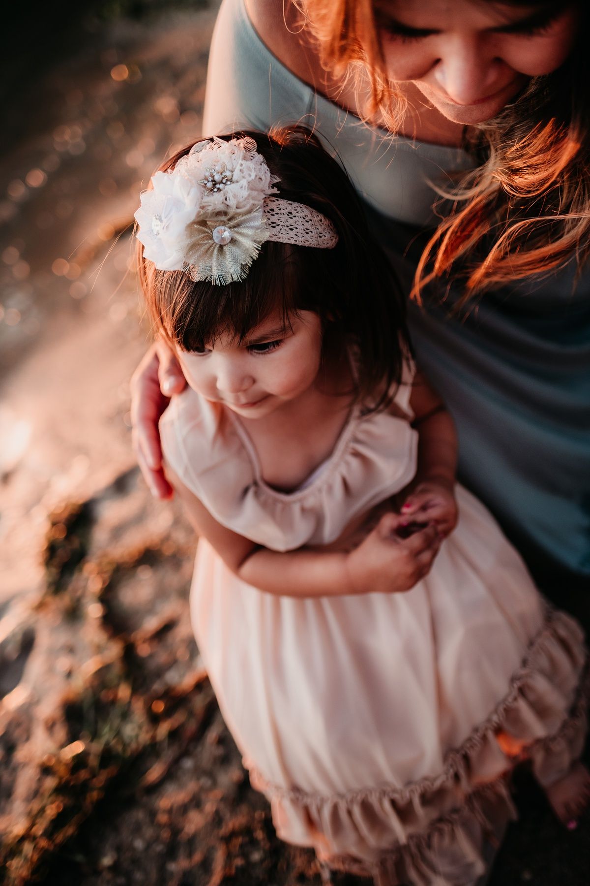 Close-up portrait of parent and child in pink dress with white flower headpiece at sunset.