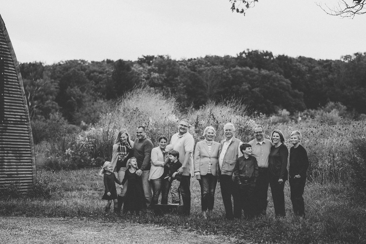 A large family group poses together outdoors in a black and white photo with trees in the background.