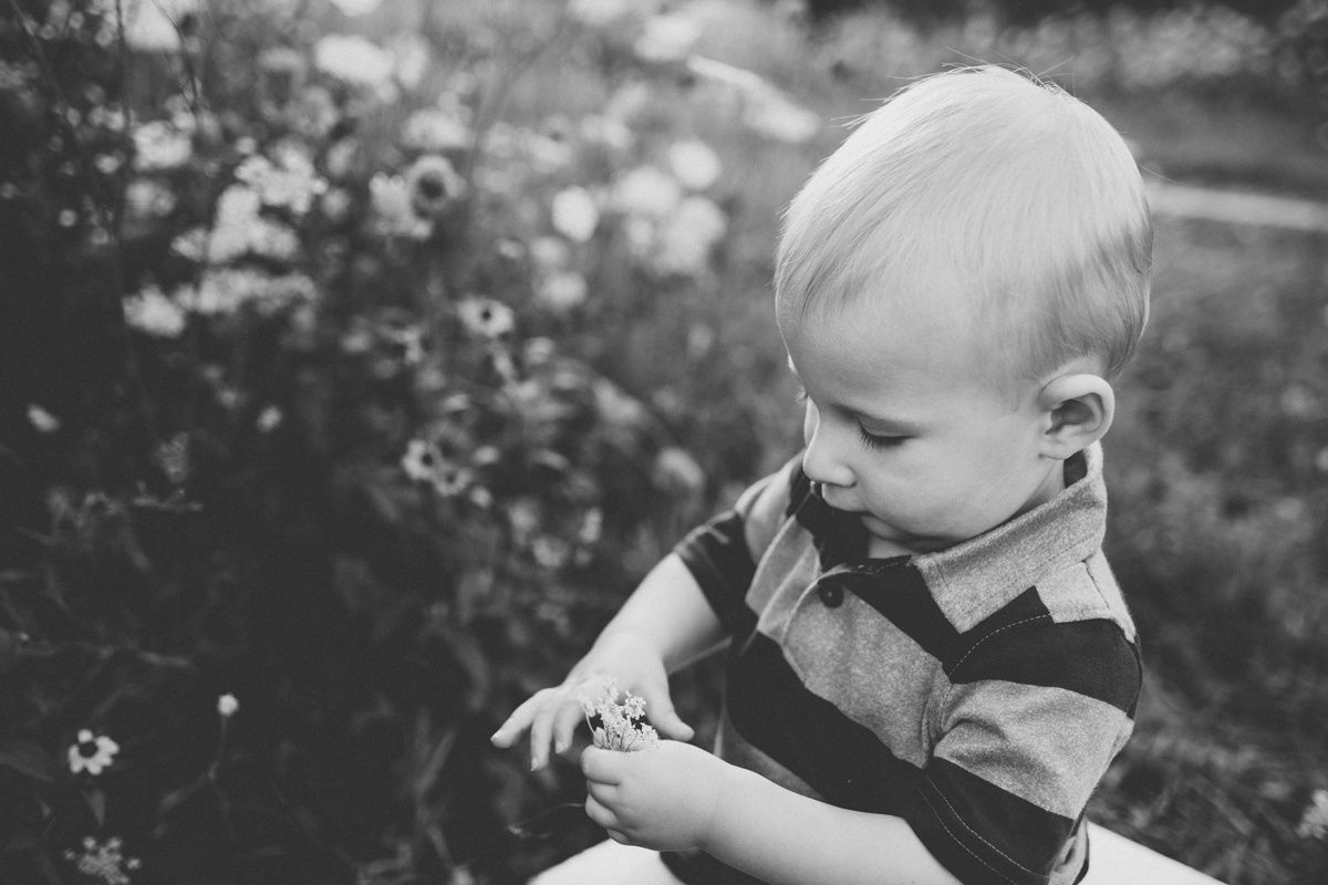 Black and white portrait of a small child sitting outdoors examining something in their hands.