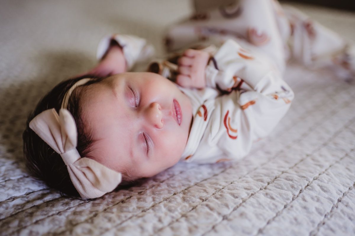 Sleeping newborn baby wearing a pink bow and floral outfit on textured bedding.