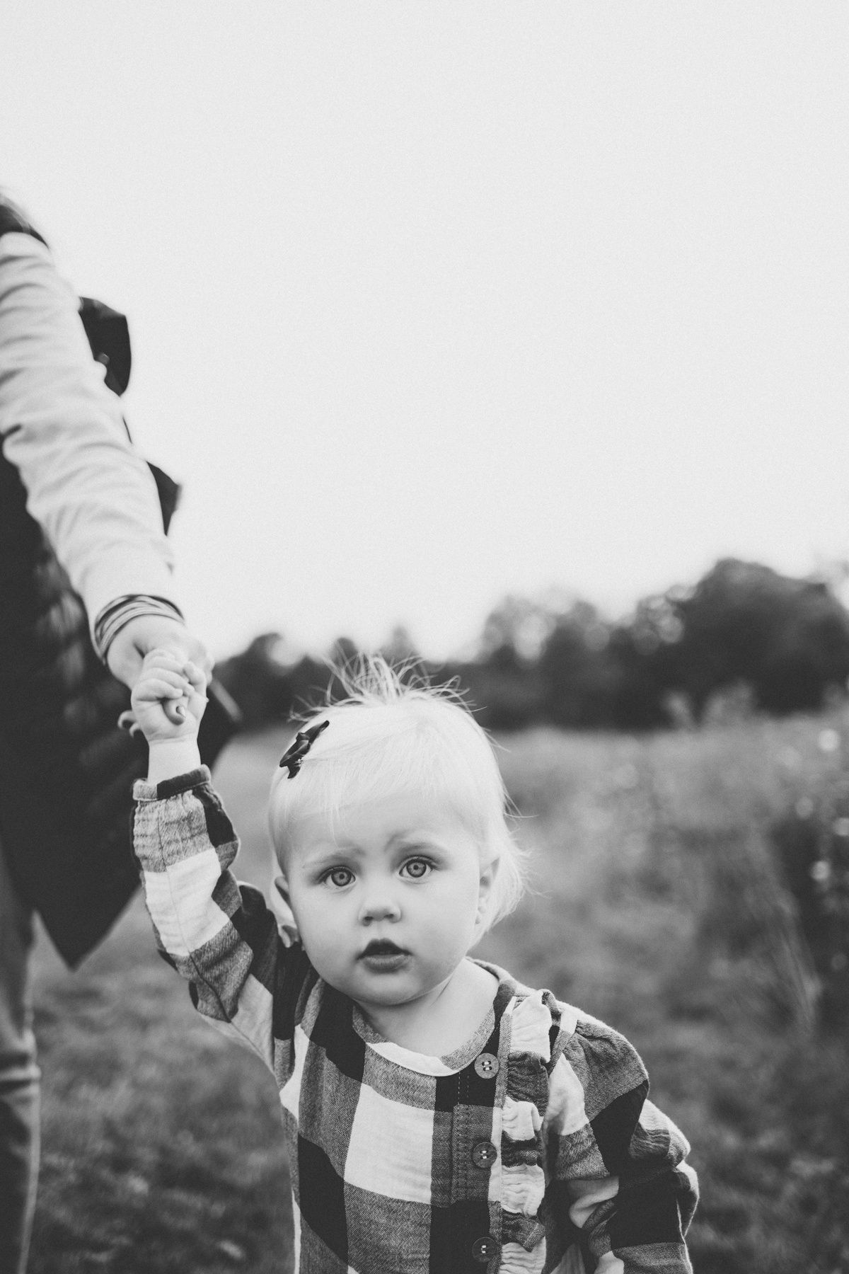 Black and white image of child holding hand while standing in field.
