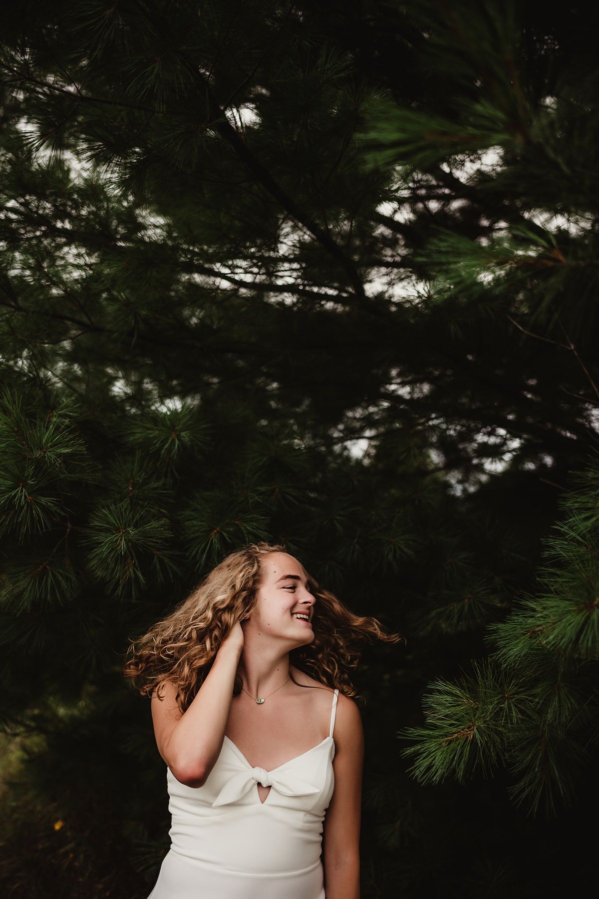 Joyful movement portrait against dark pine trees with flowing hair.