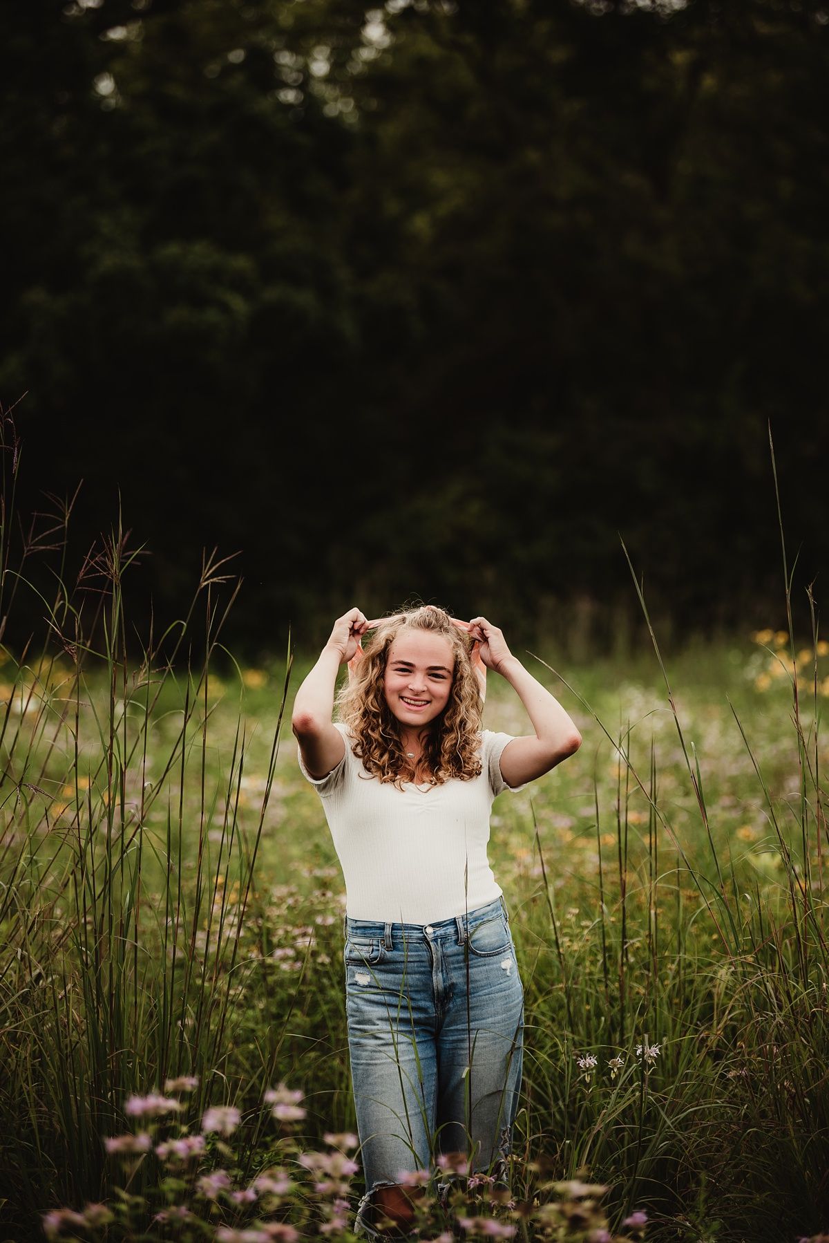 Playful outdoor portrait surrounded by tall grasses and wildflowers.