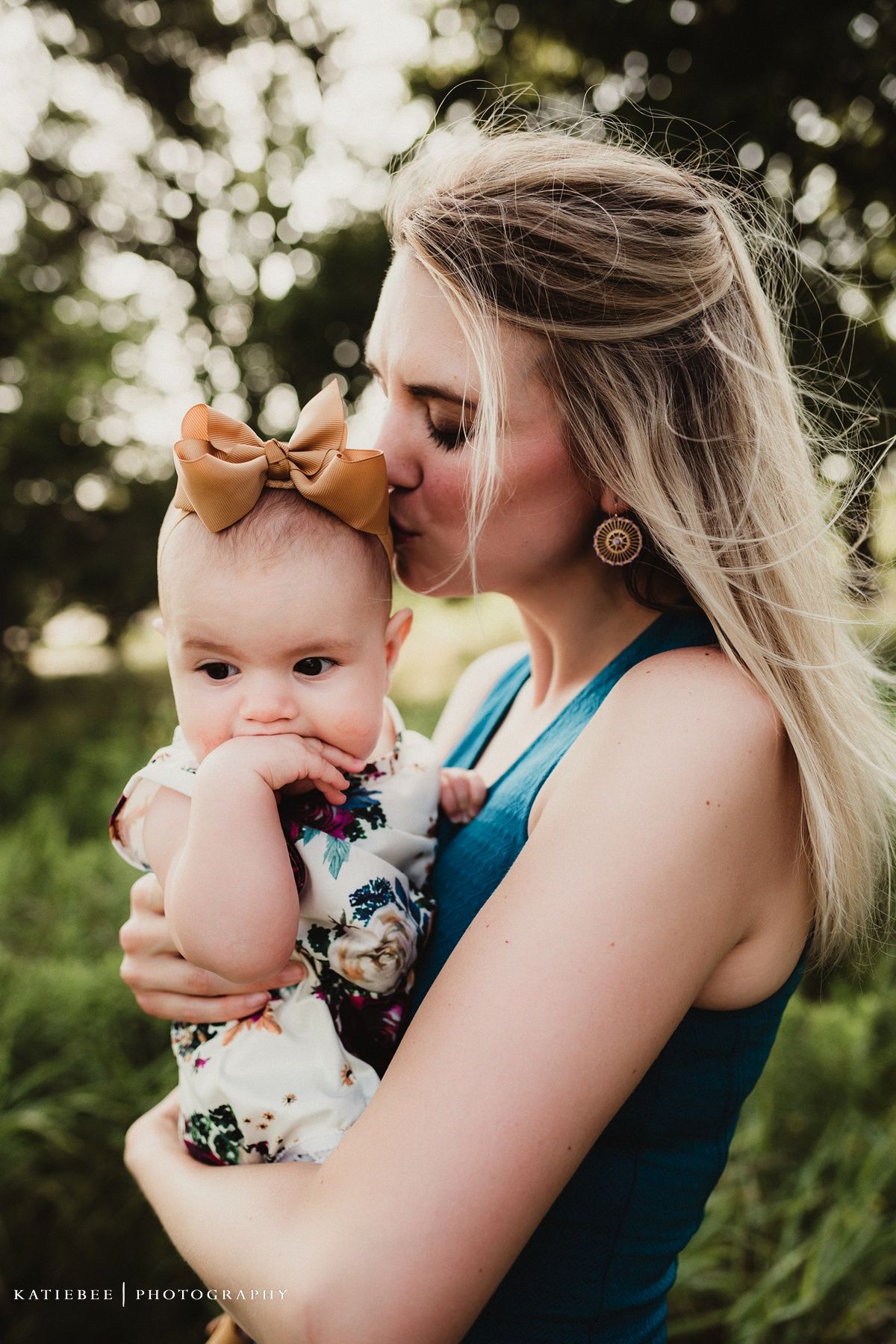 An intimate outdoor moment captured between parent and baby wearing a tan bow against a dreamy bokeh background.