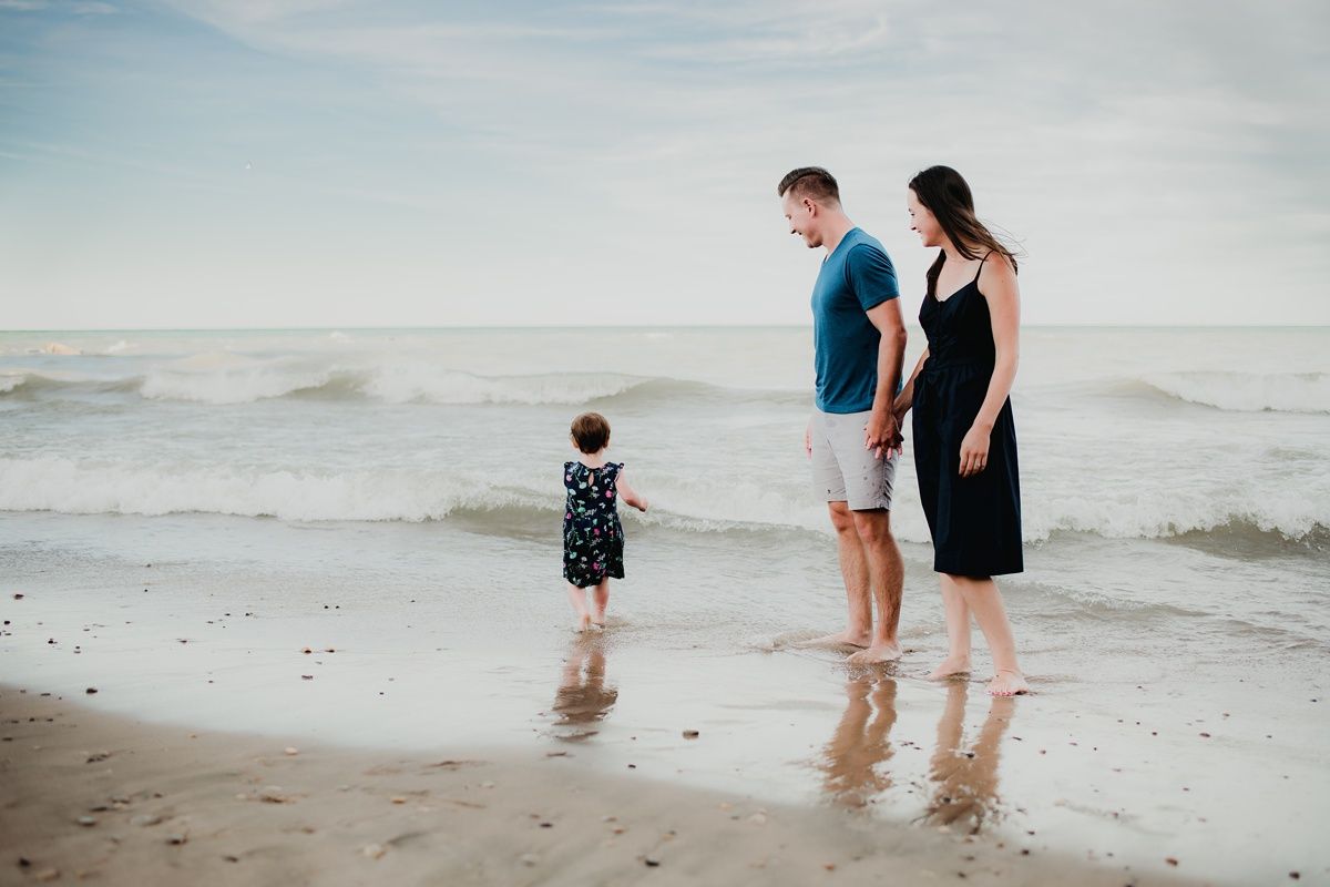 A family stands together in the shallow surf watching the ocean waves roll in.