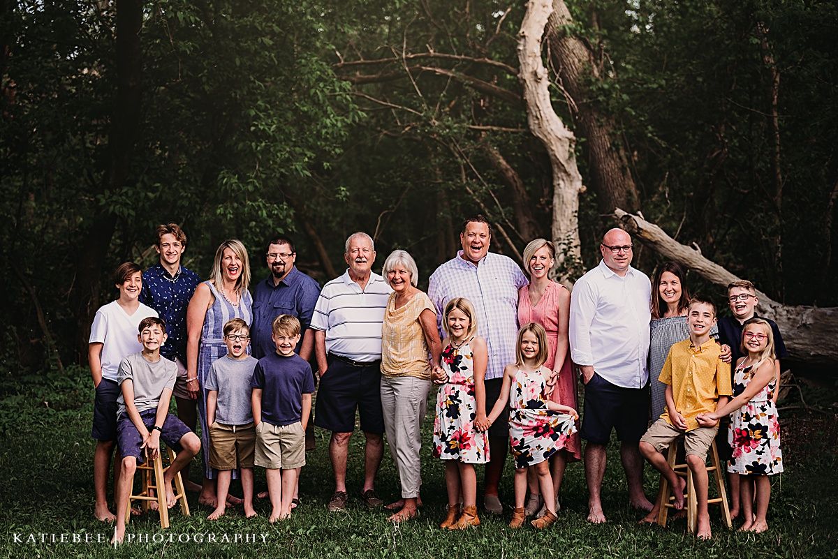 Extended family gathering poses for group photo on grassy lawn with forest backdrop.