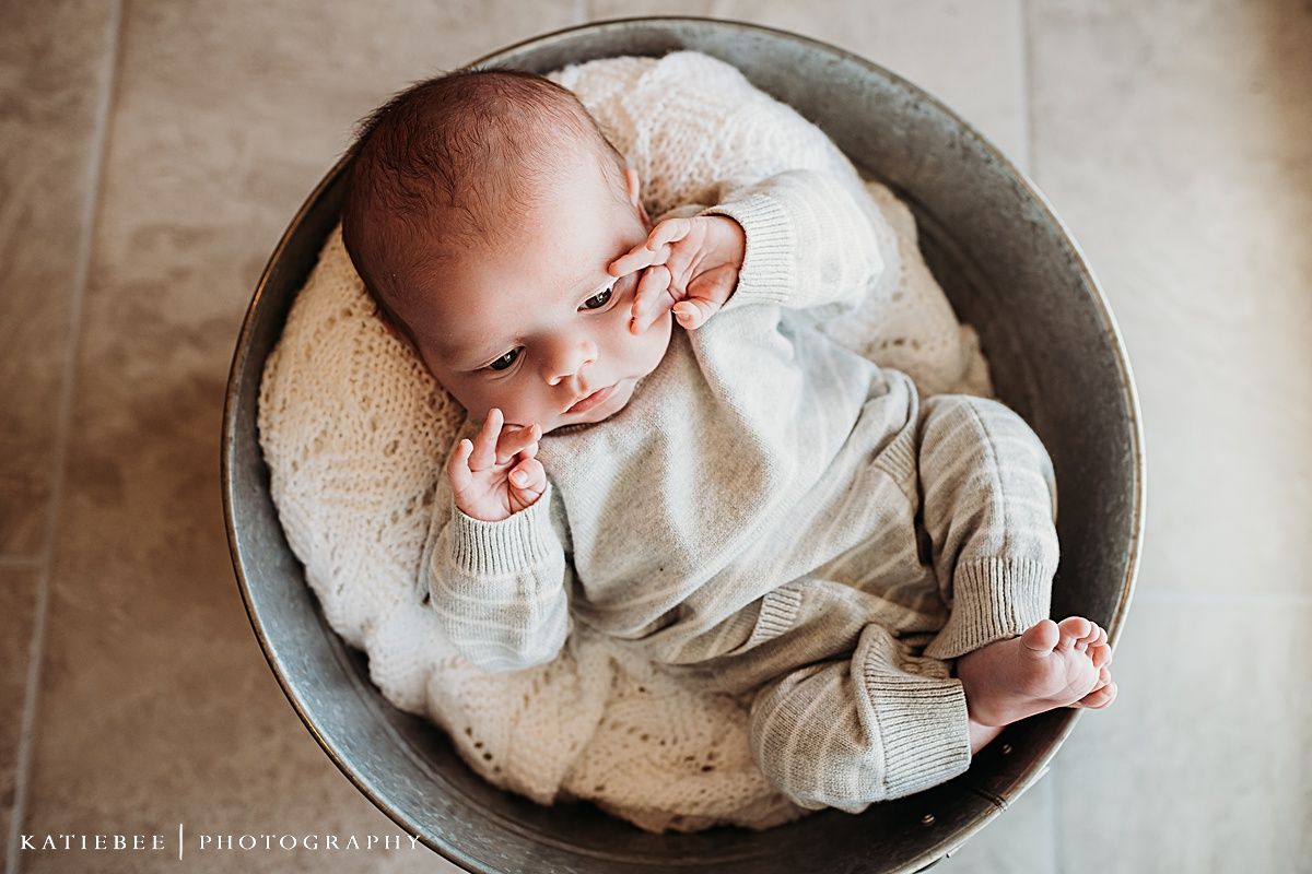 Peaceful baby resting in round metal basin on white blanket.