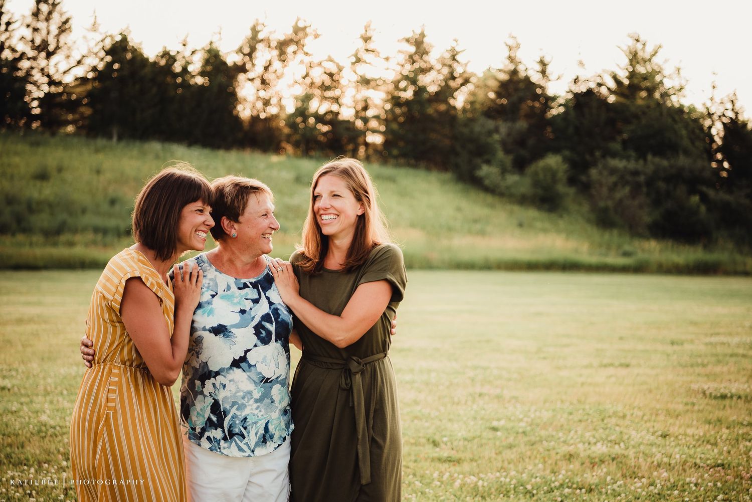 Three friends sharing laughter and embracing outdoors during sunset.