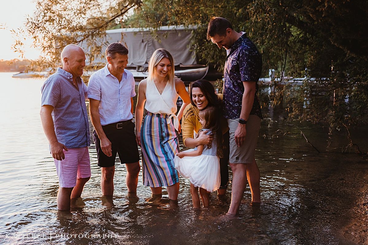 Casual gathering of people standing in shallow water at sunset near a dock.