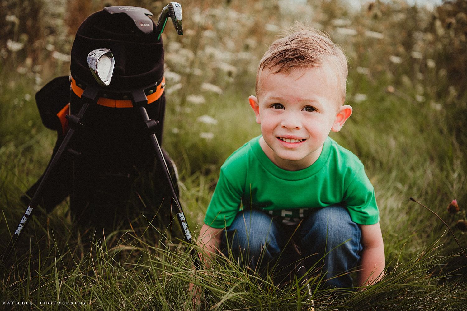 A plush black penguin toy sits beside a child in a bright green shirt in a grassy field.