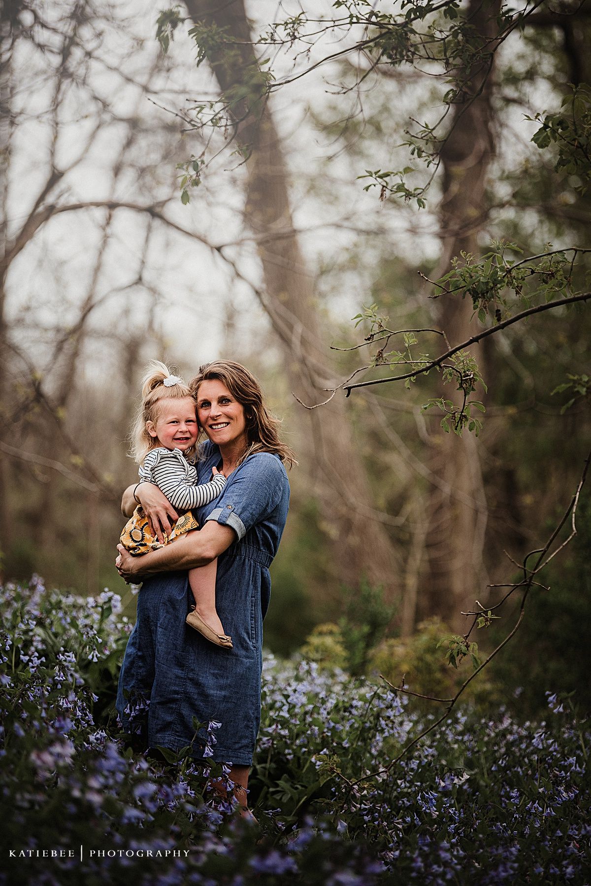 Beautiful outdoor family portrait in a forest with blooming purple wildflowers at dusk.