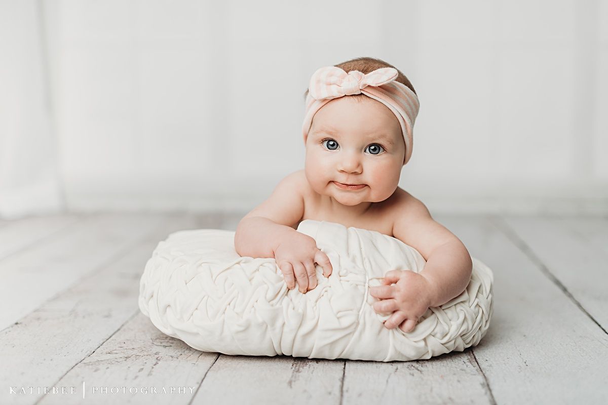 Baby wearing a pink headband sitting on a white cushion during a light and airy photography session.