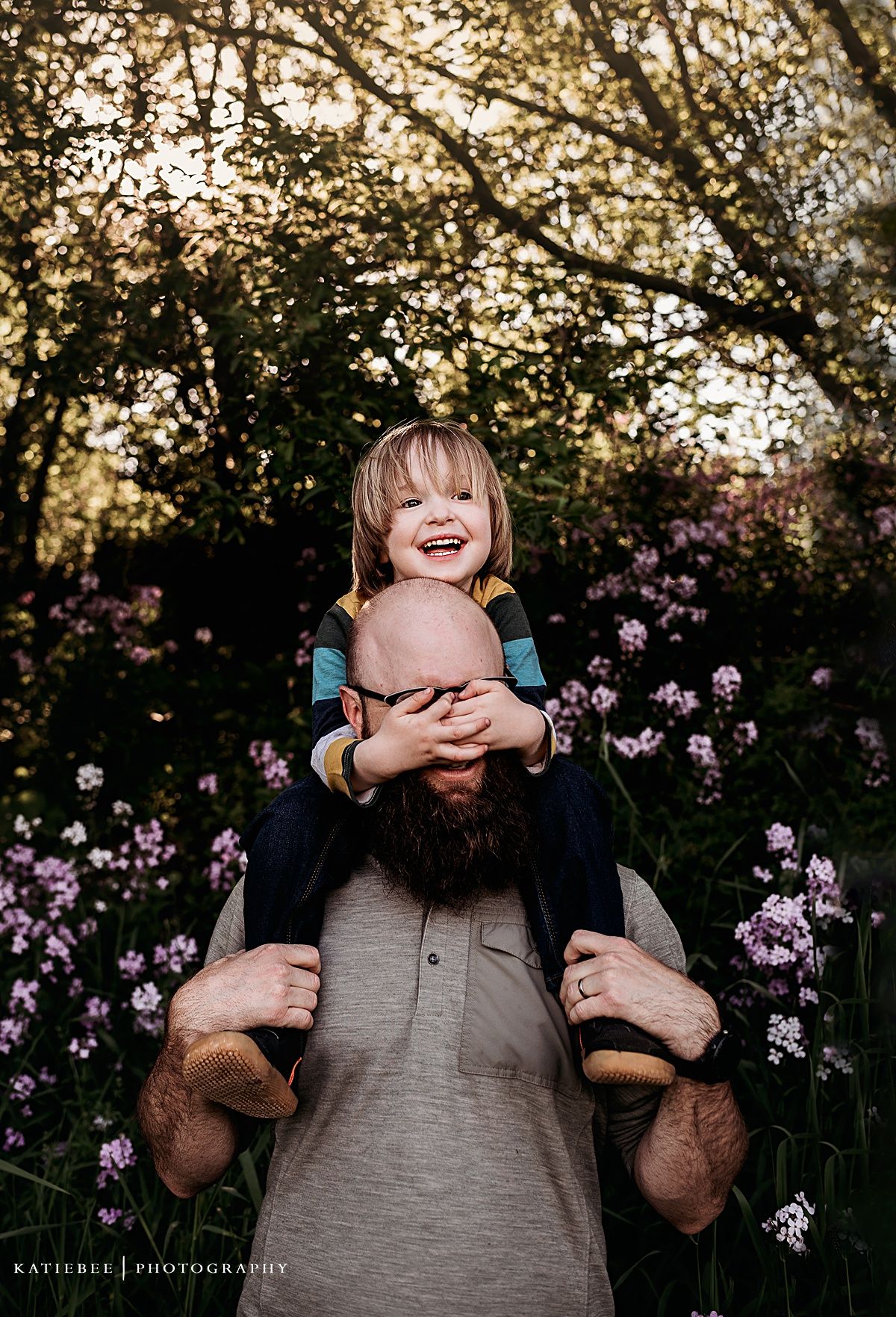 Playful outdoor portrait with purple flowers and golden sunlight filtering through trees.