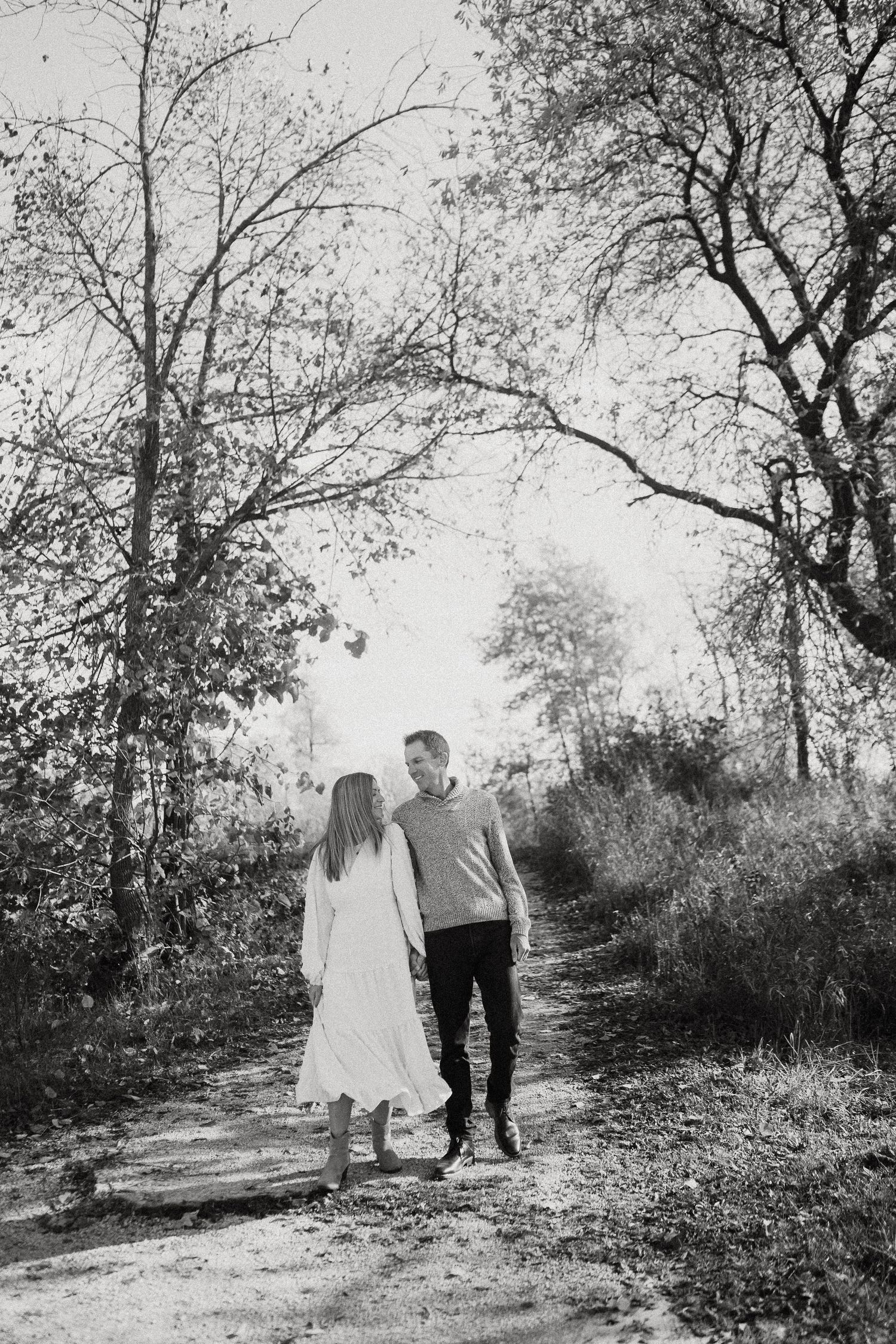 A series of black and white photographs capturing a couple walking together along a tree-lined trail.