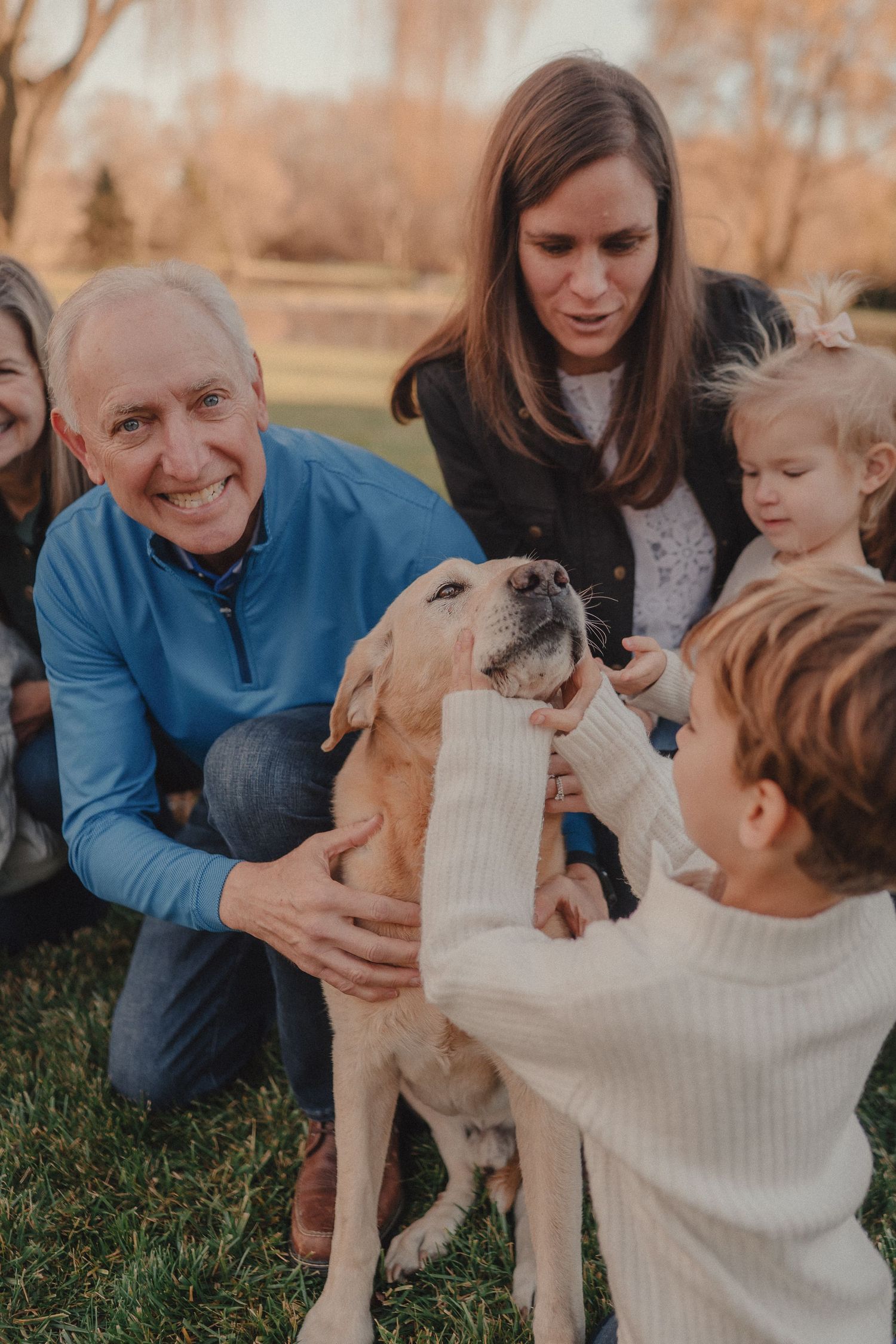 A dog gets attention and pets from a group gathered outdoors on a fall day.