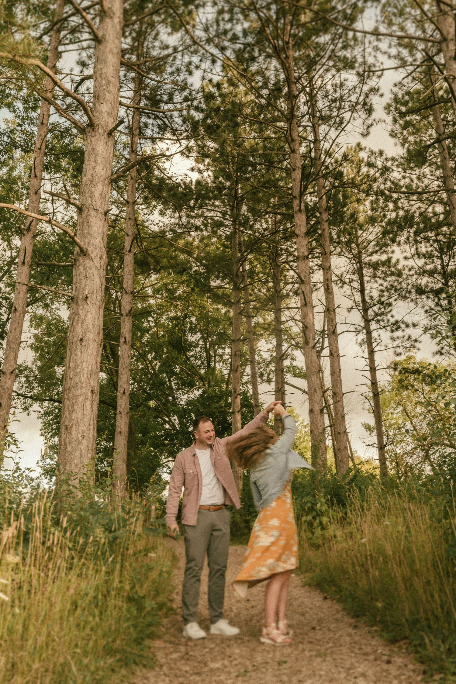A couple walks along a pine tree-lined trail during a warm sunset.
