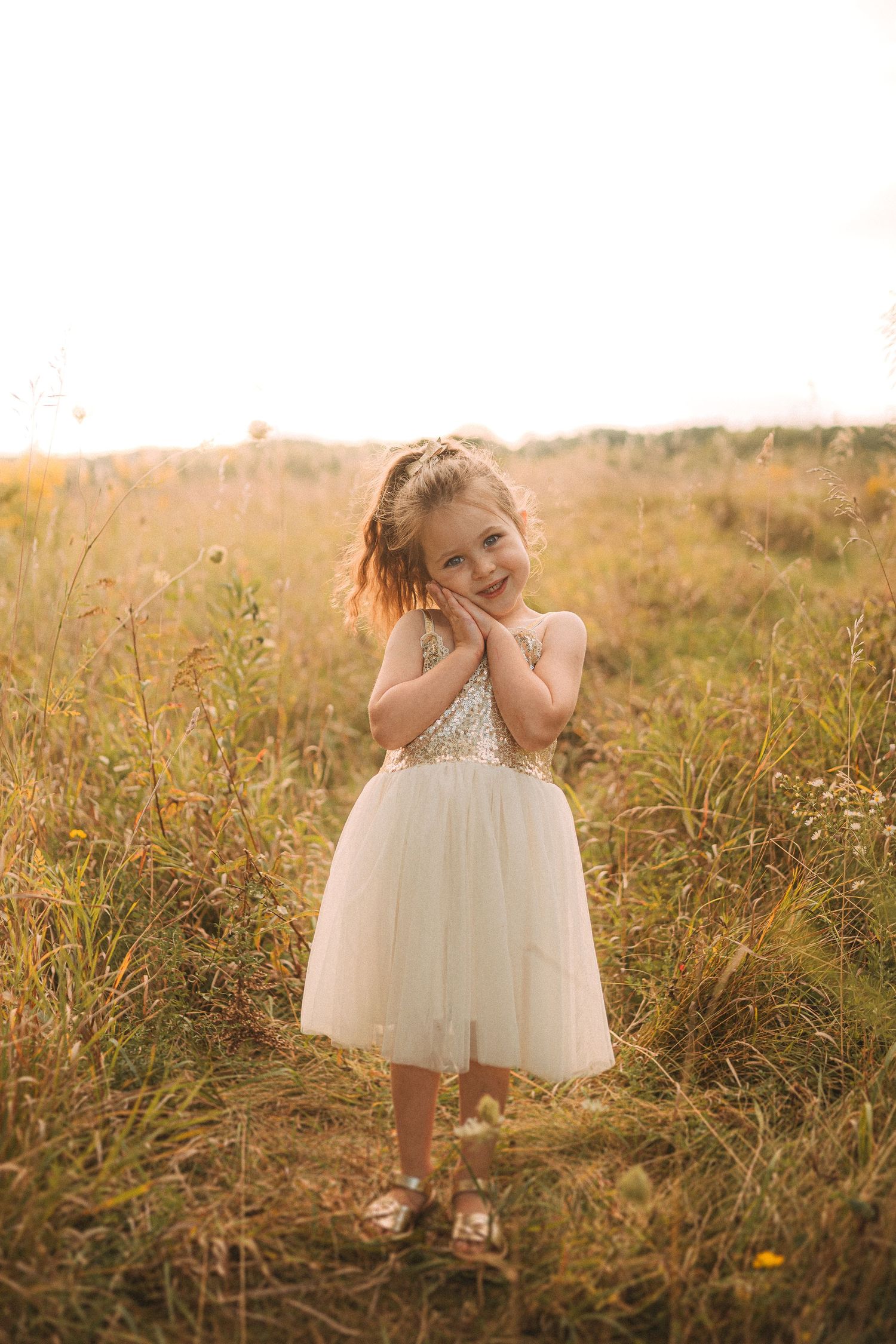Young girl in white tulle dress posing in golden sunlit field.