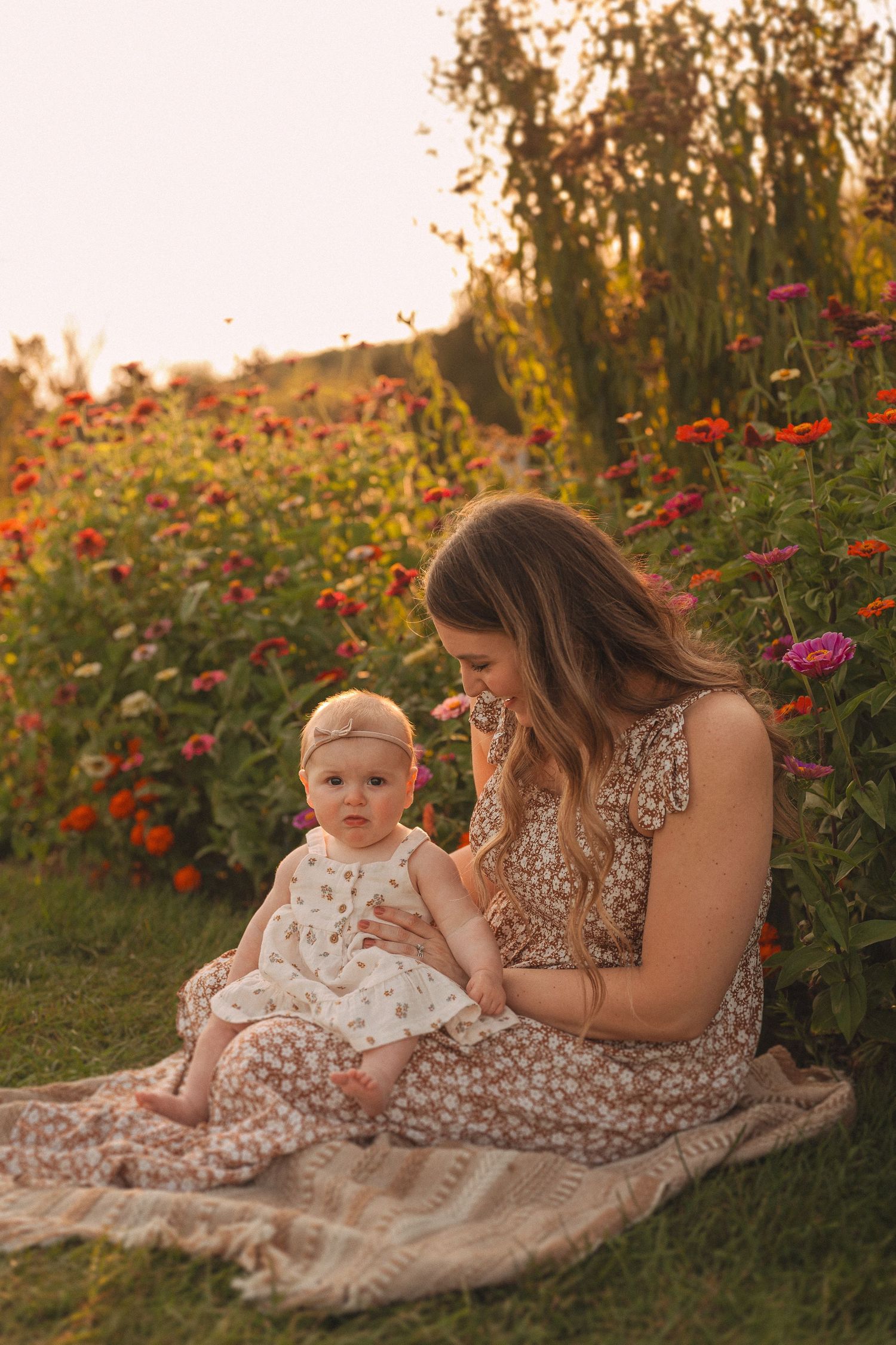Sunset garden scene with matching floral dresses on blanket among colorful zinnias.