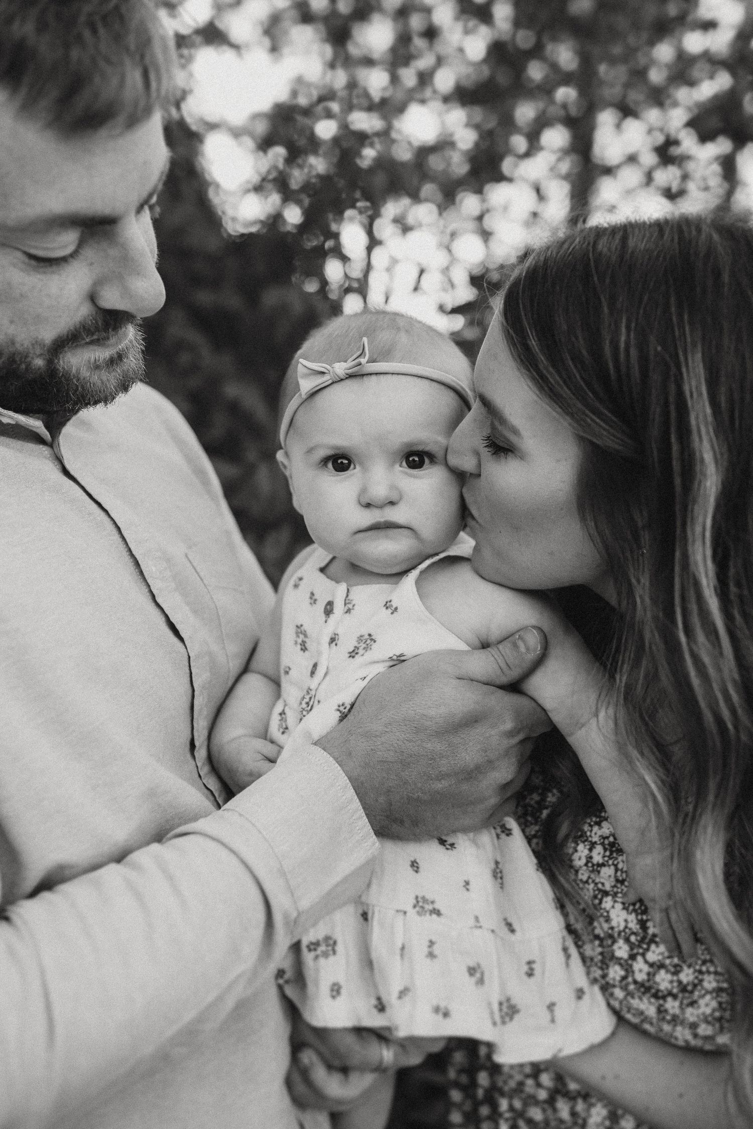 An intimate black and white portrait of a young family sharing a tender moment outdoors.