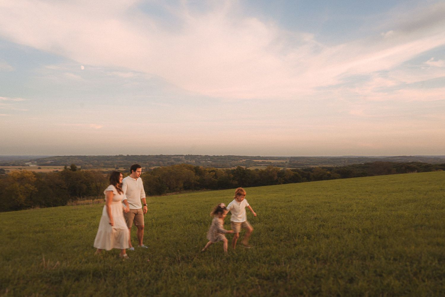 Family running and playing together on a hilltop during golden hour.