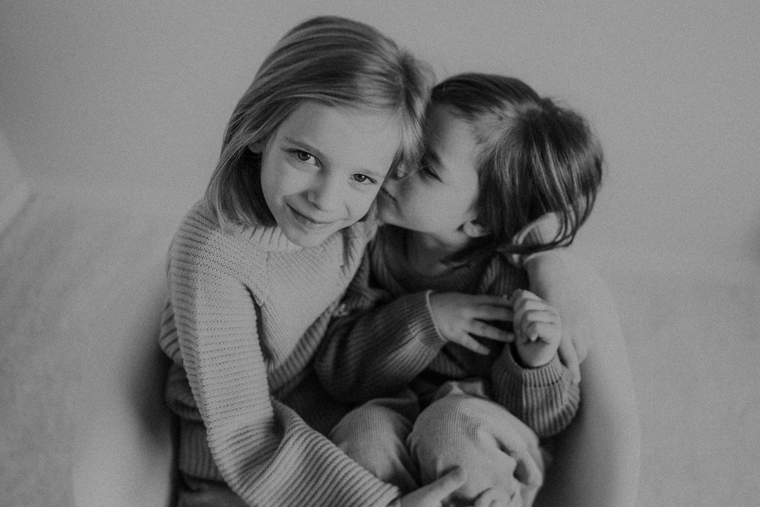 Two playful children share a sweet moment in a black and white portrait while wearing cozy sweaters.