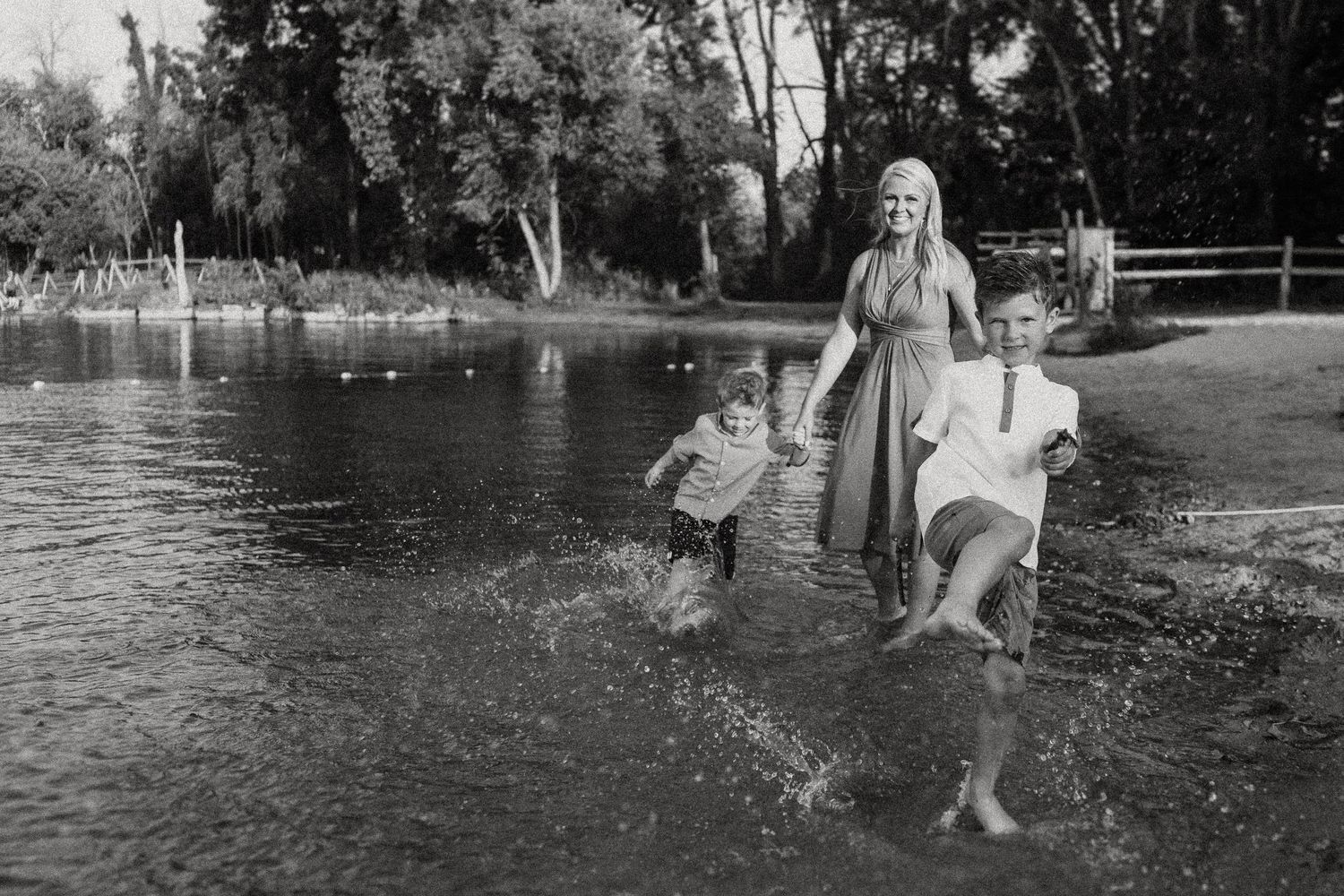 A joyful black and white photo of people splashing in shallow water by a lake.