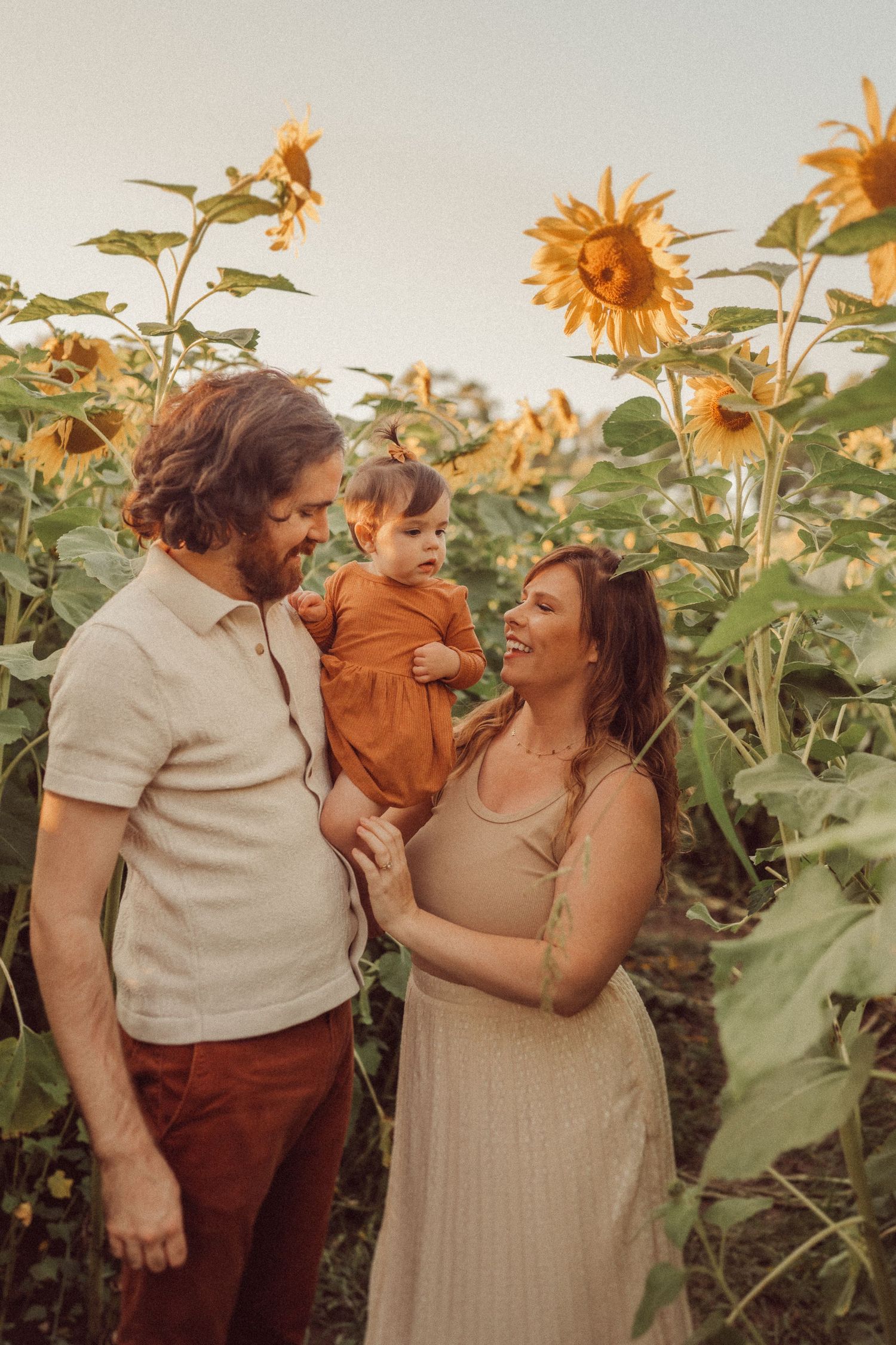 Family sharing a tender moment among towering sunflowers at sunset.