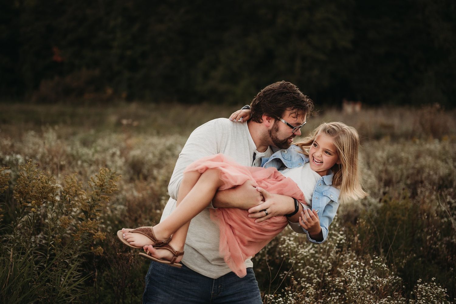 A playful moment captured as one person lifts another in a field during golden hour.
