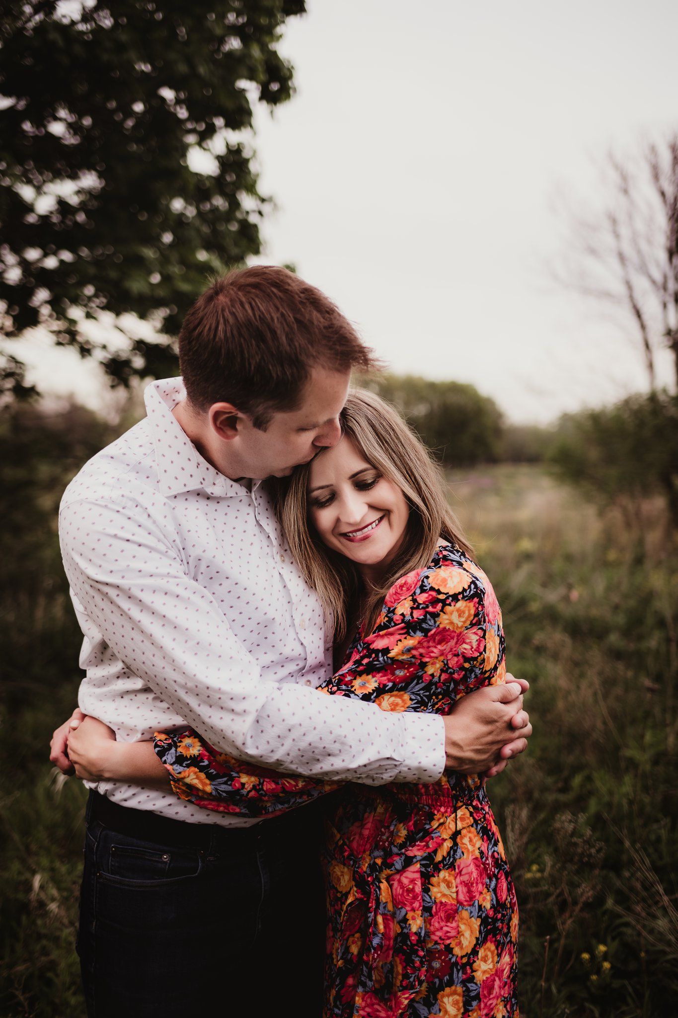 A couple embraces in a field during golden hour wearing coordinated outfits.