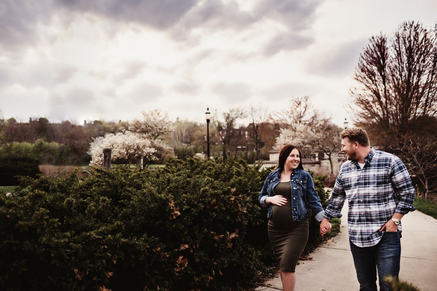 Casual couple walking together on path with blooming trees in background.