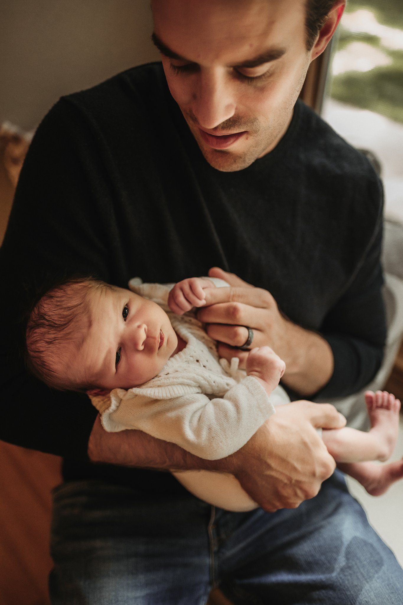 Tender moment between parent and baby wearing white onesie in warm indoor lighting.