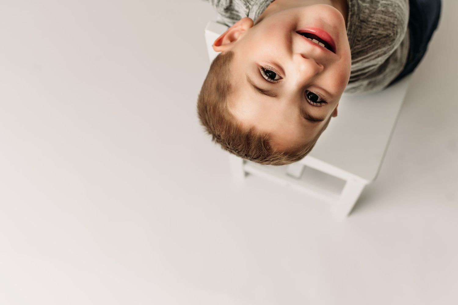 Creative upside down portrait of child in gray shirt against white background.