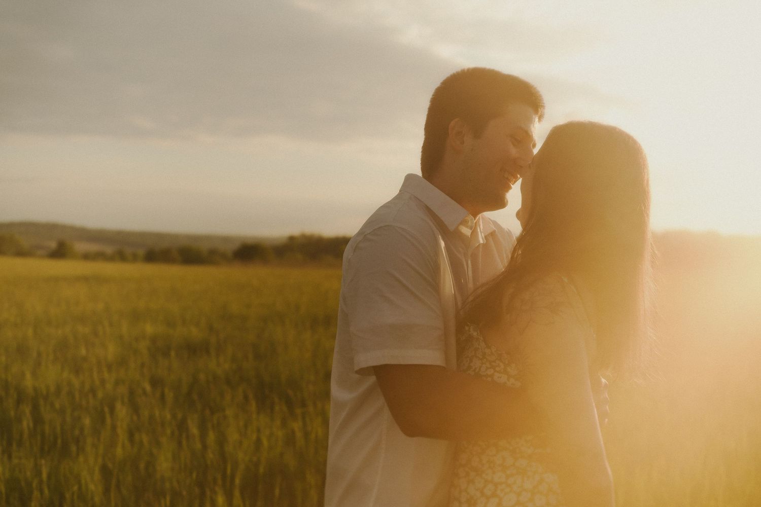 Silhouetted figures embrace in a sun-drenched field during golden hour.