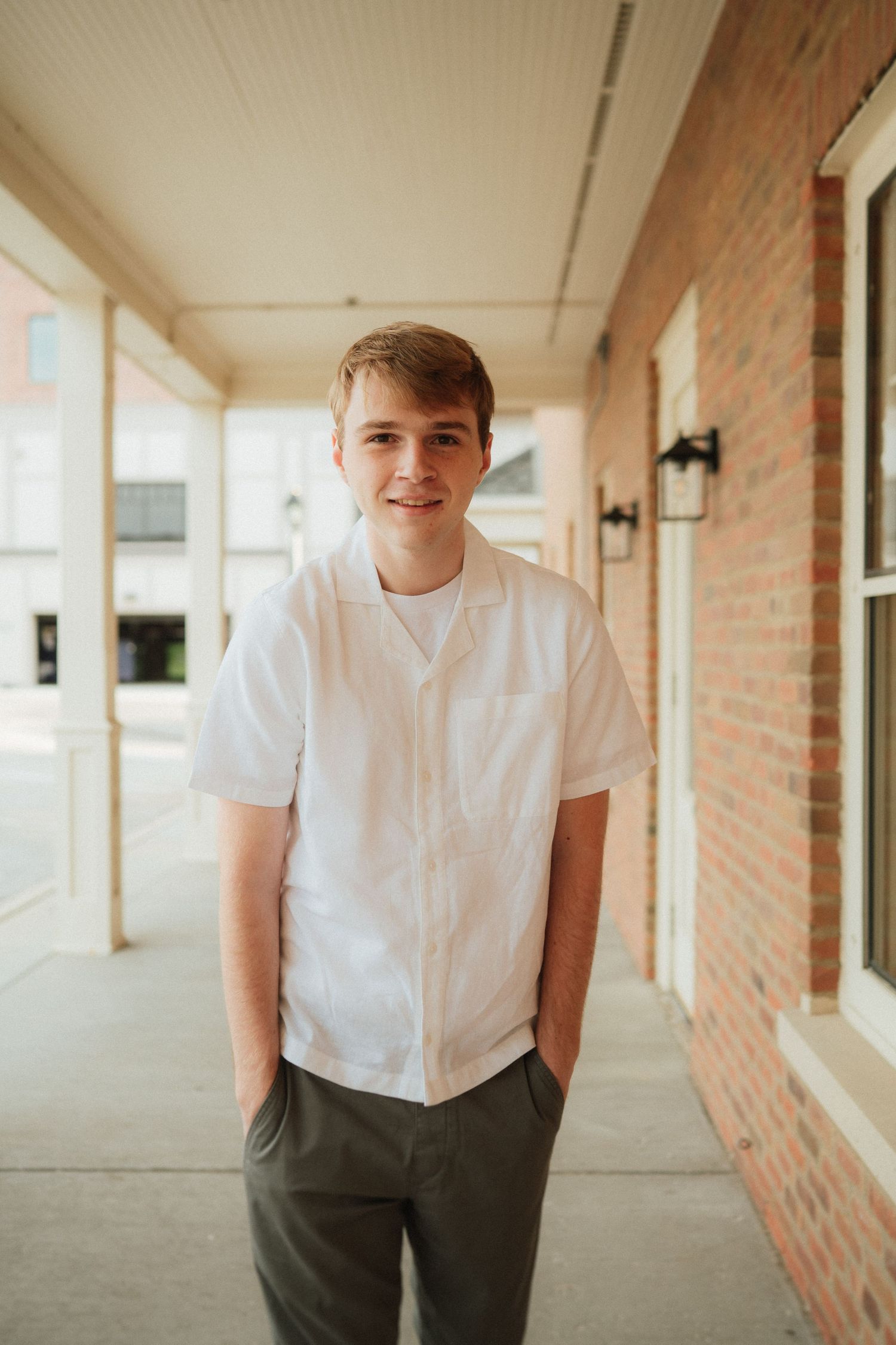 Person in white shirt and dark pants posing in front of brick corridor with natural lighting.