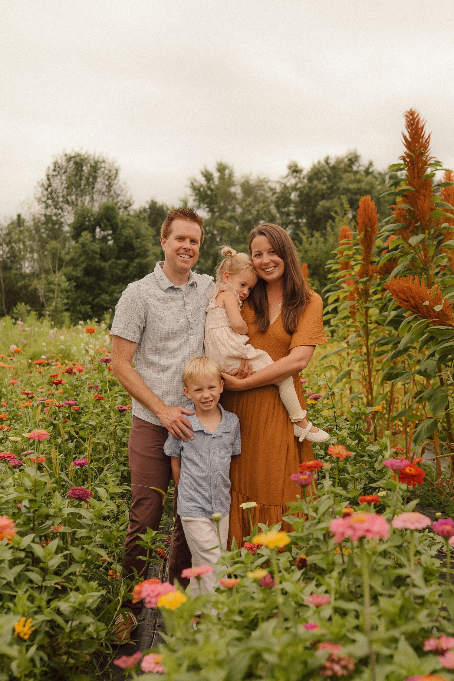 A group poses together in a garden filled with vibrant flowers and tall orange plants on a summer evening.