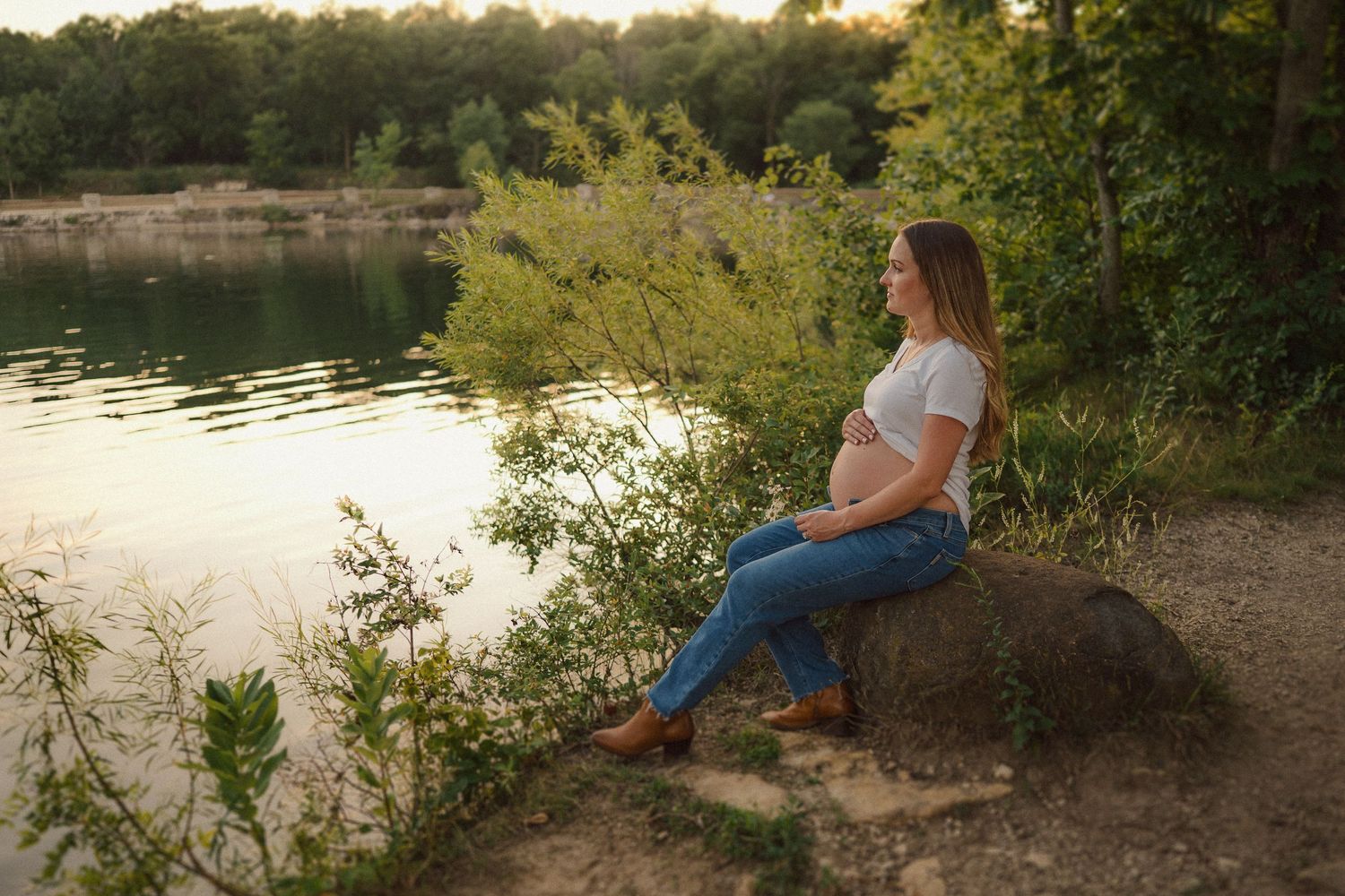 A romantic couple sits together on a rock overlooking a serene lake at sunset.
