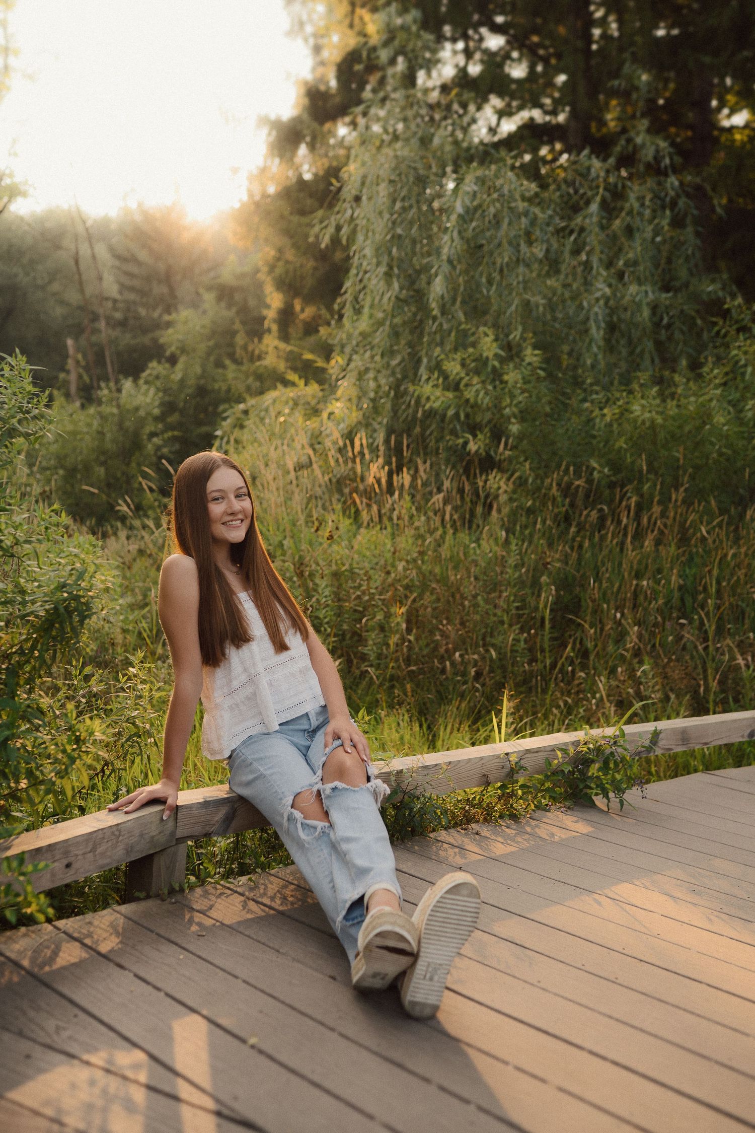 Person relaxing on a wooden deck surrounded by lush summer greenery at golden hour.