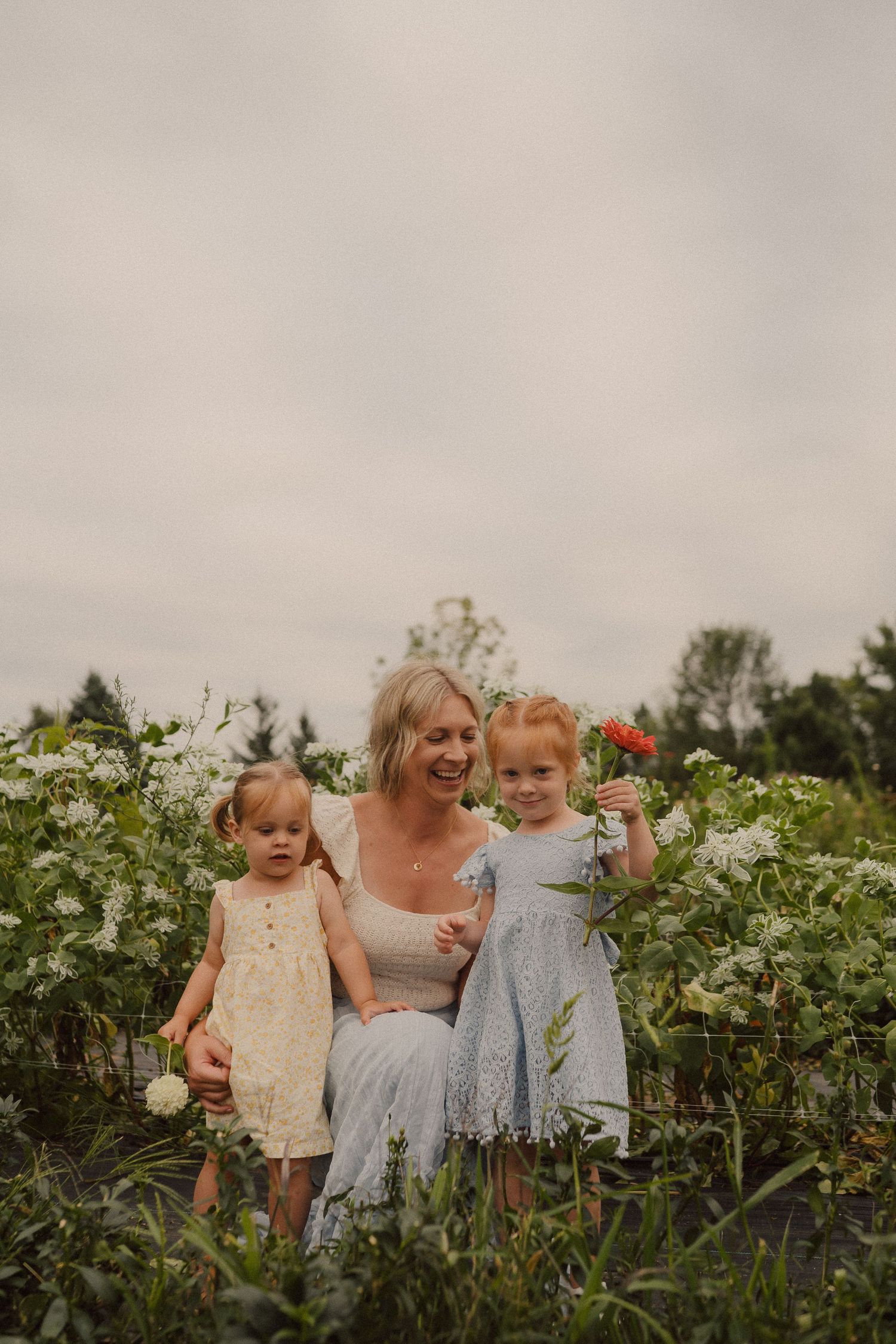 Family members smiling together in a lush green garden surrounded by blooming plants and flowers.